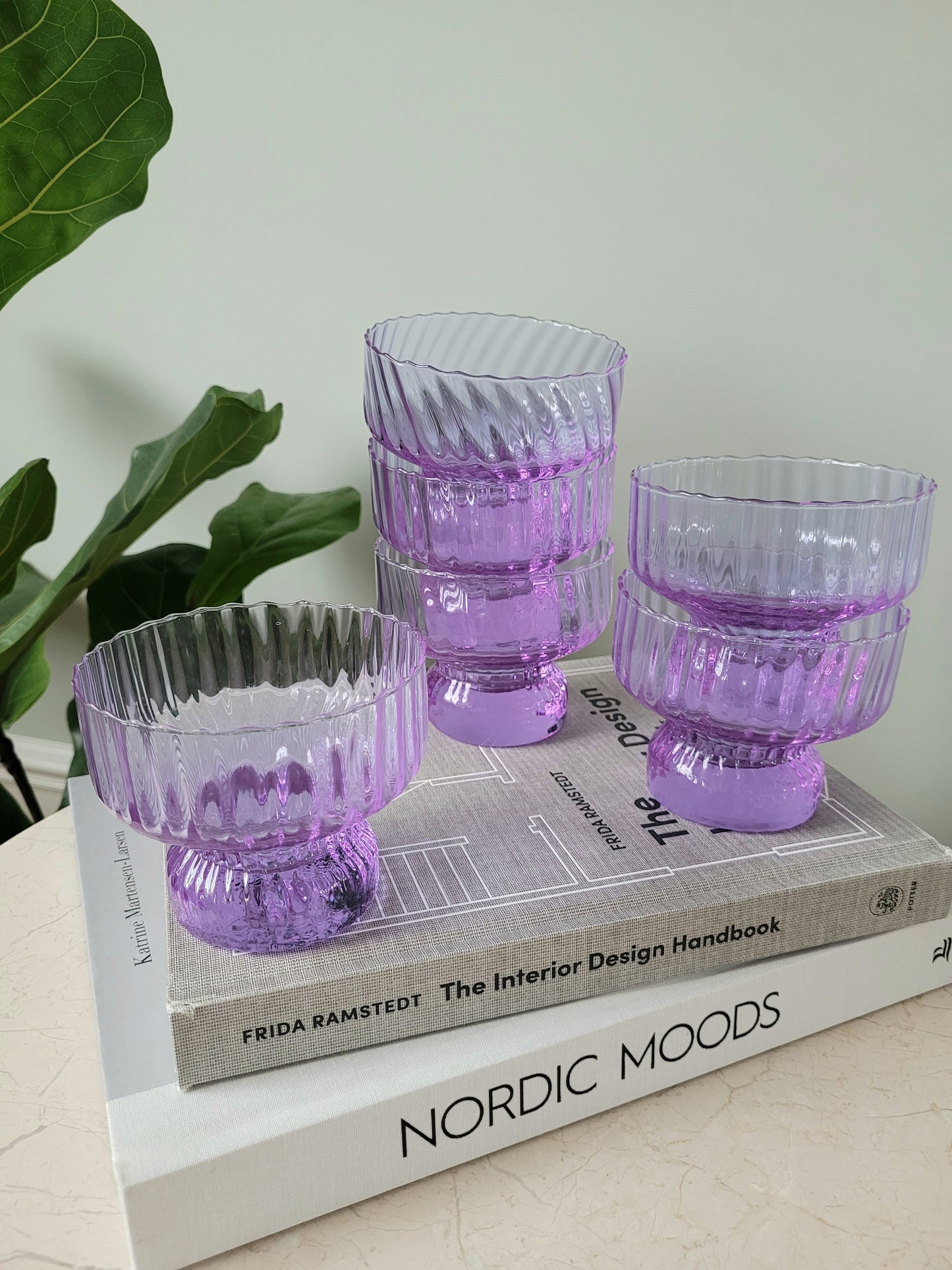 full view of six purple Italian glasses and cups on a stack of interior books