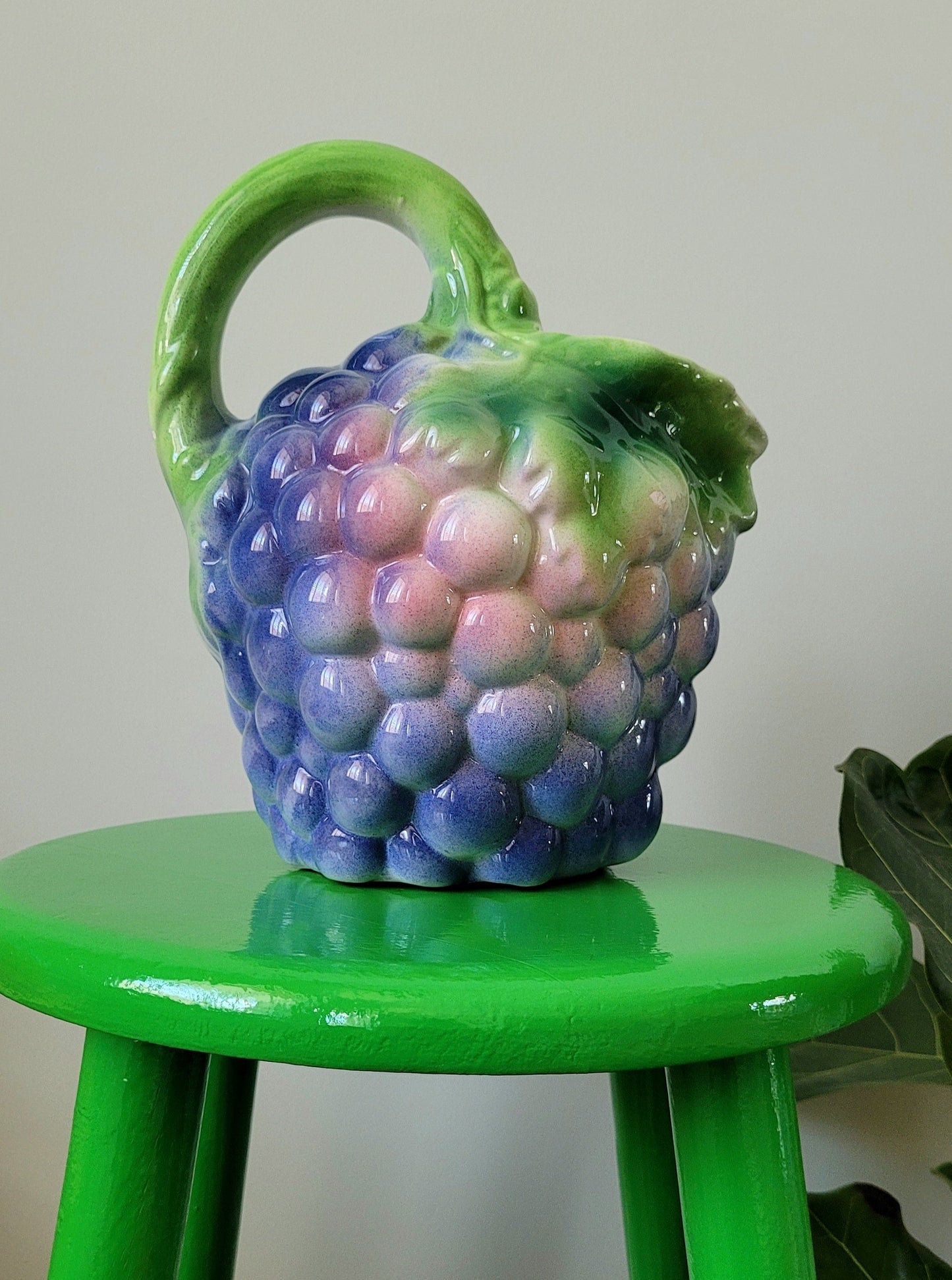 side view of a barbotine ceramic wine pitcher with grapes on a green side table