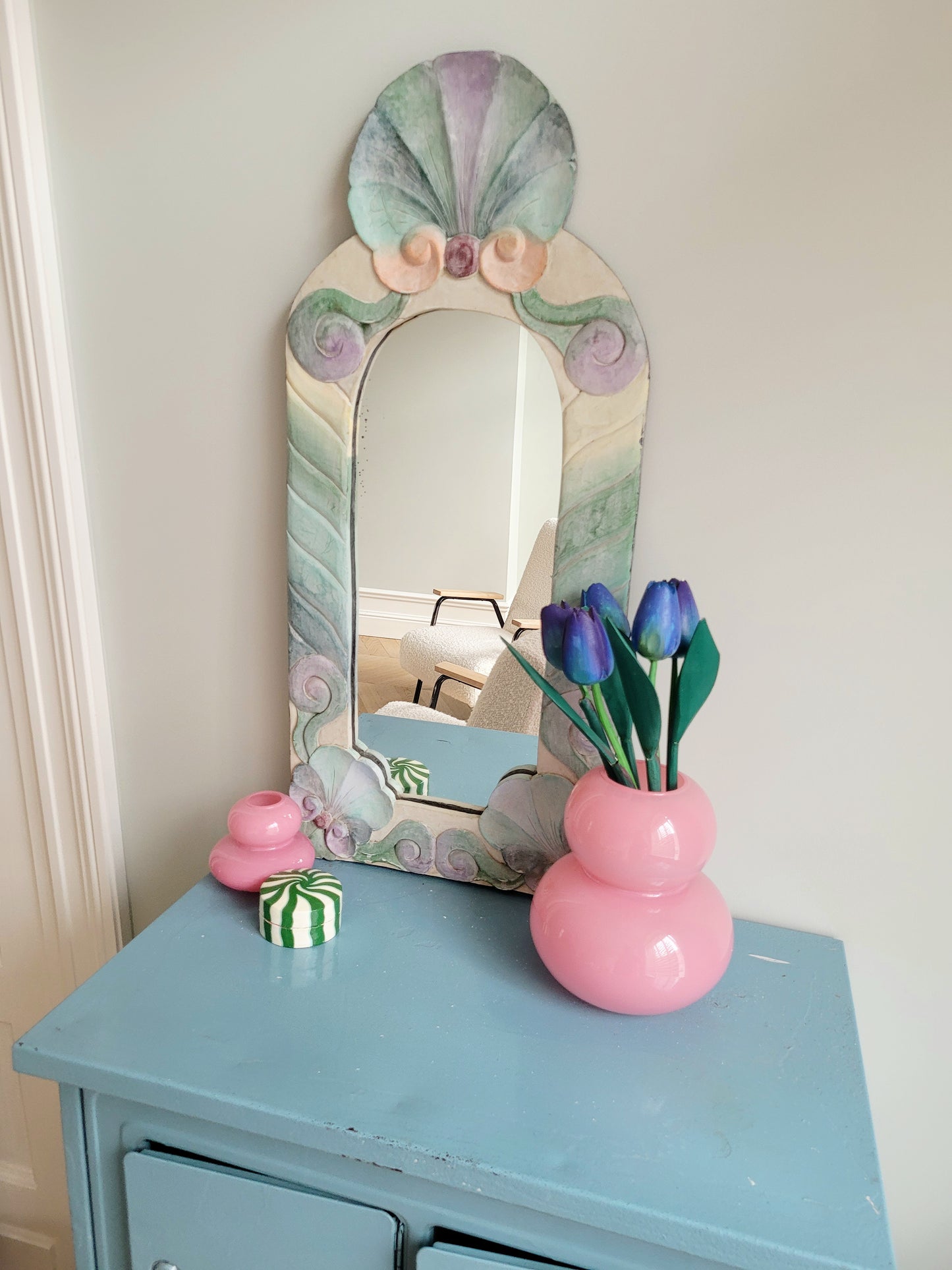side view of a pastel coloured wooden wall mirror with flower design next to a pink vase with wooden tulips