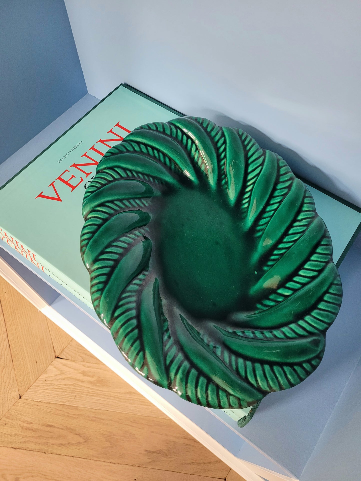 top view of a vintage green ceramic plate on a blue shelf