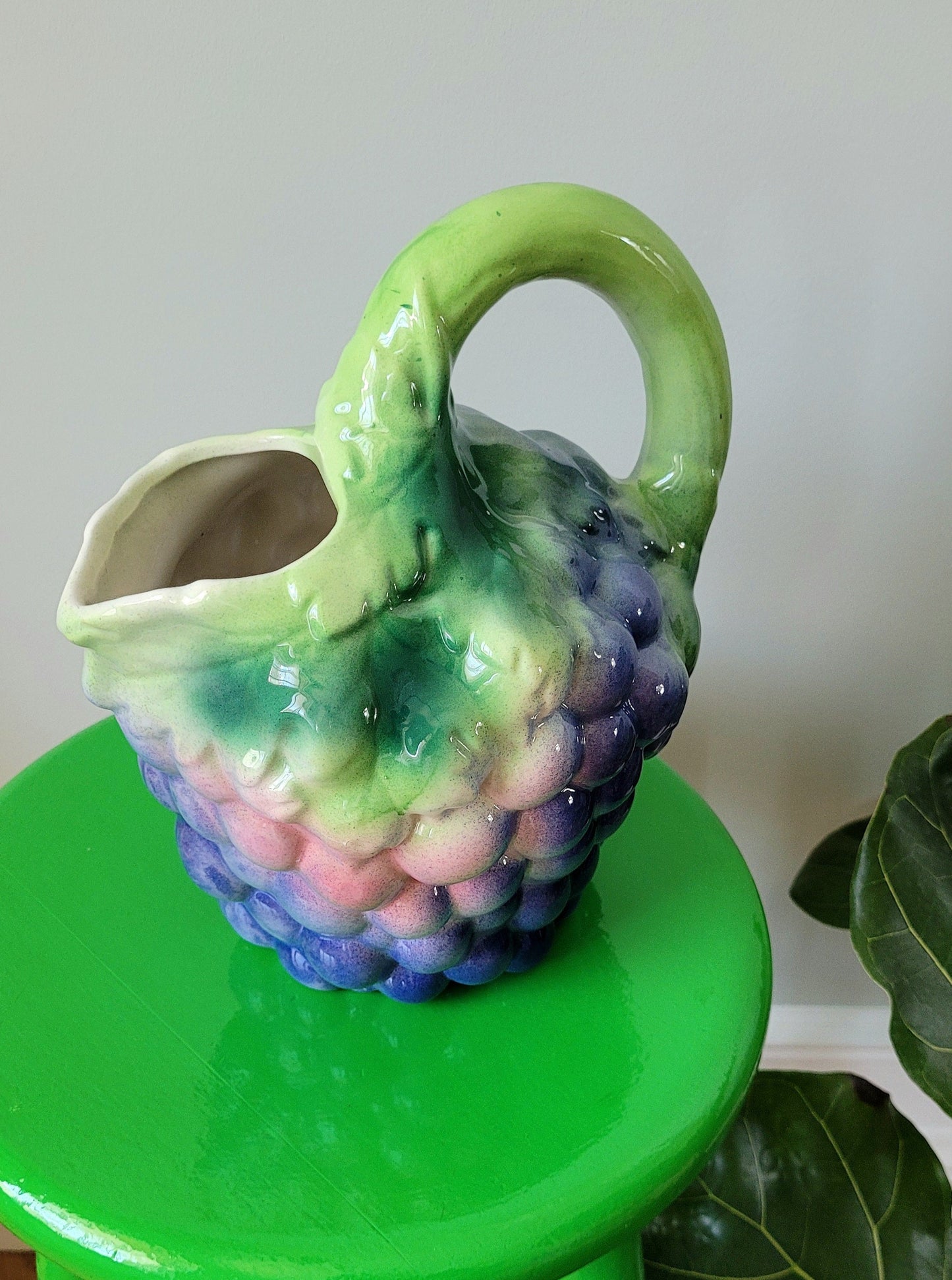 top view of a barbotine ceramic wine pitcher with grapes on a green side table