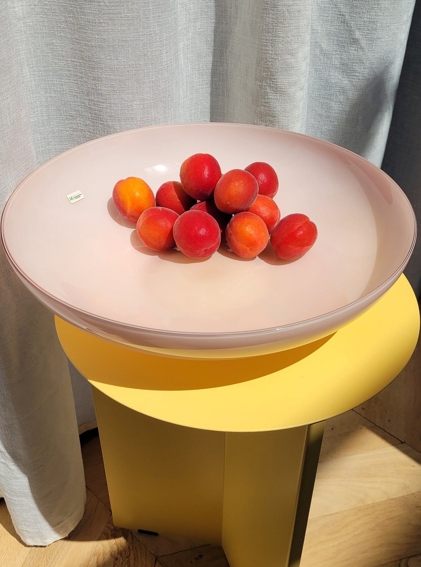 top view of a large vintage opal pink Murano bowl filled with fruit on a yellow side table