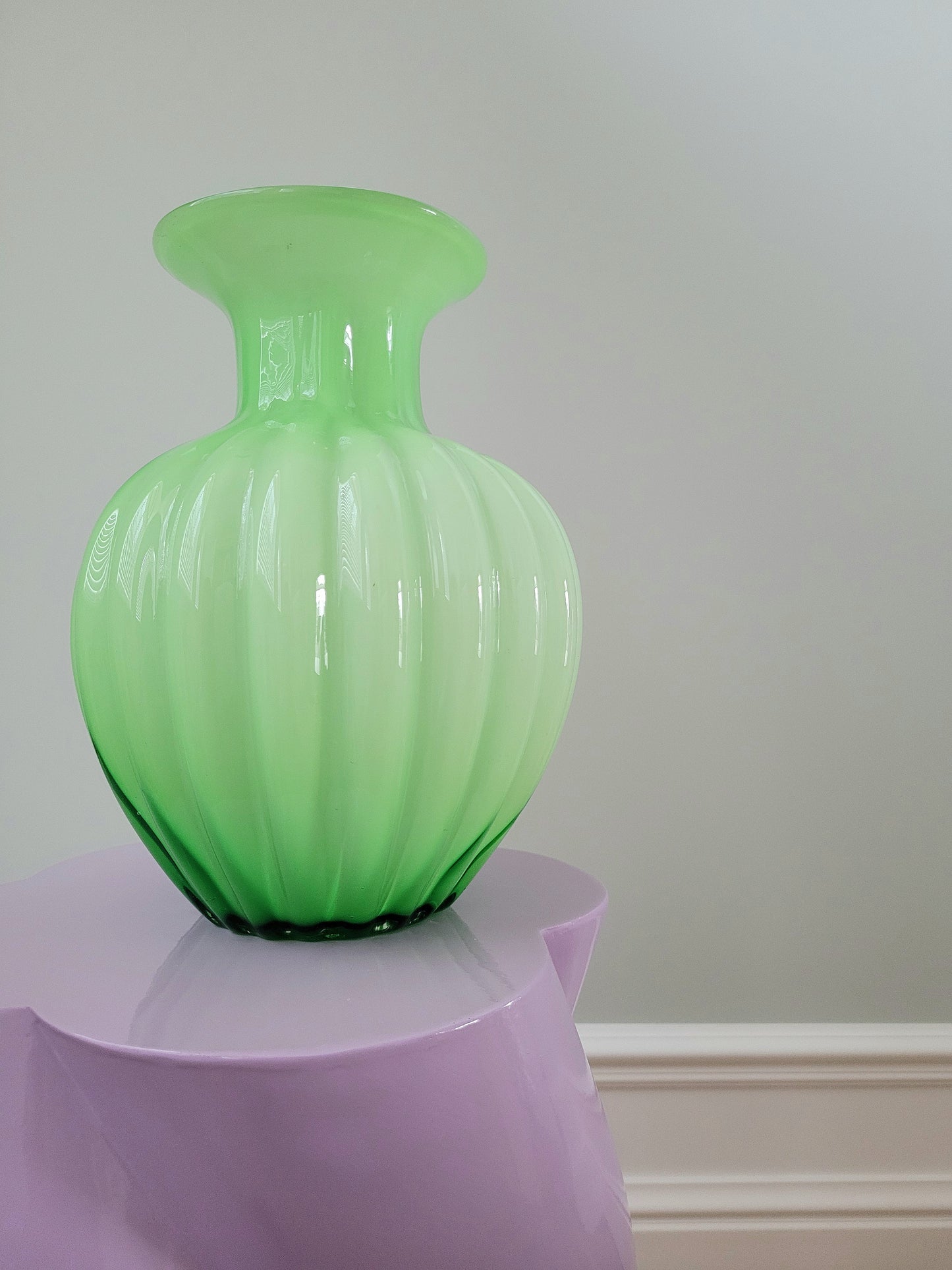 front view of a vibrant green glass vase on a purple side table