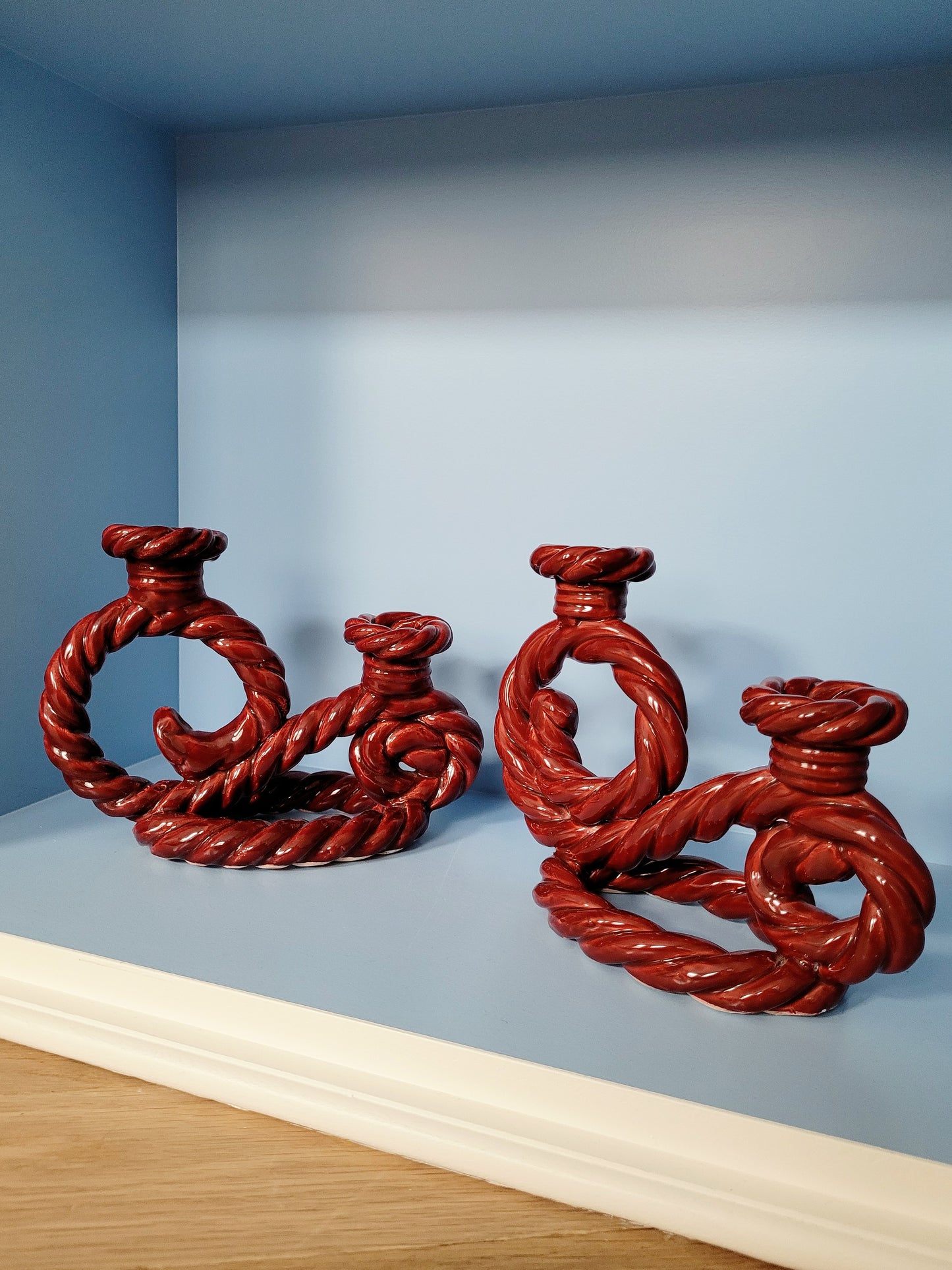 front view of two vintage red twisted ceramic candle holders in a blue cabinet
