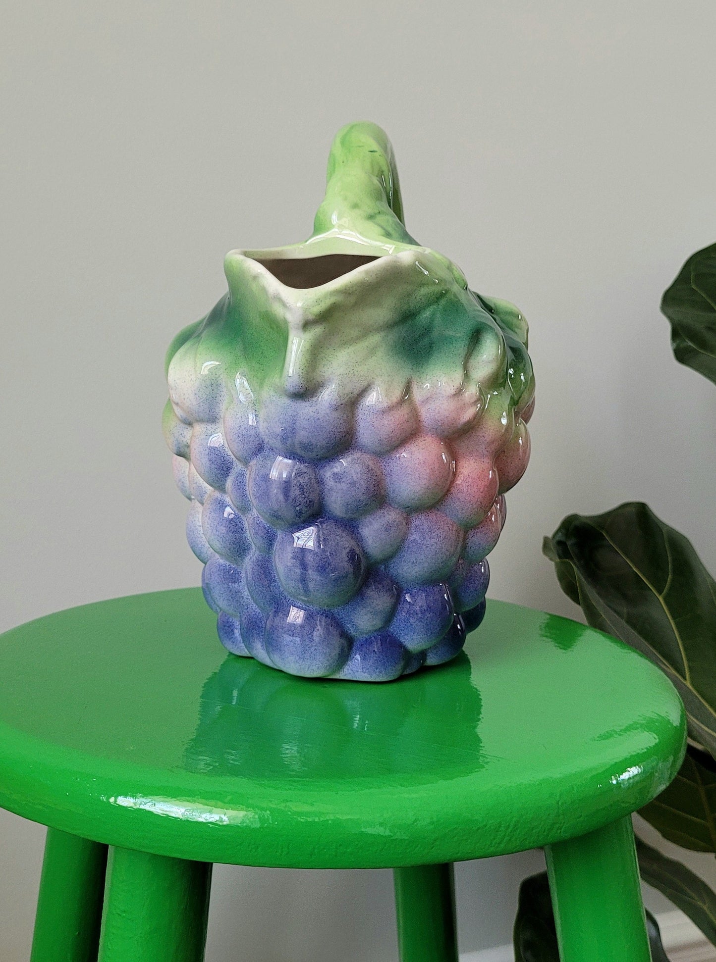 front view of a barbotine ceramic wine pitcher with grapes on a green side table