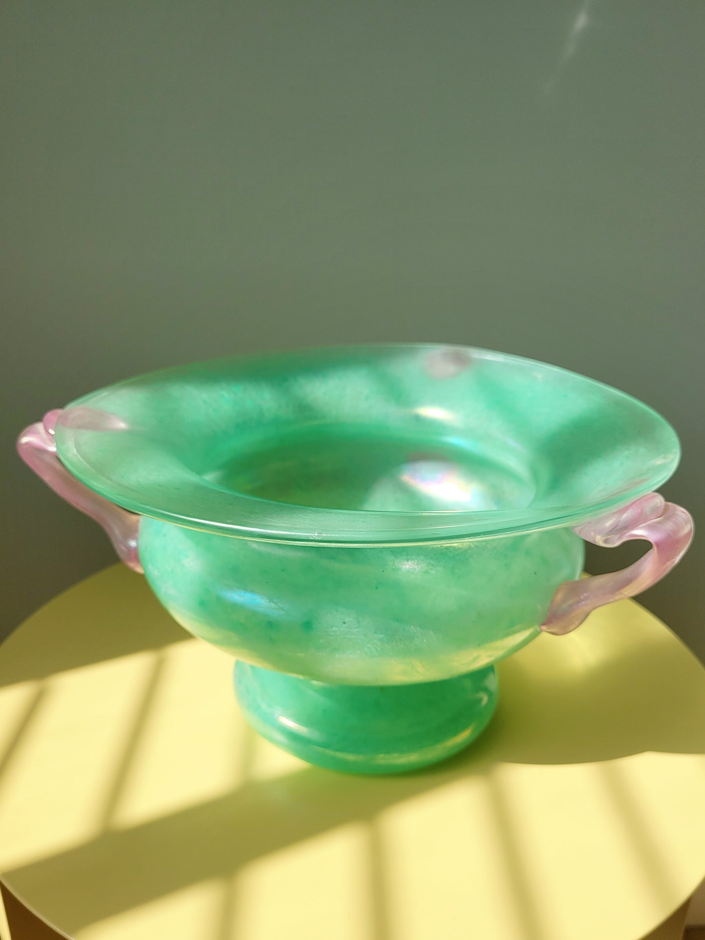 top view of a scavo Murano glass amphora vase in green and pink on a yellow side table