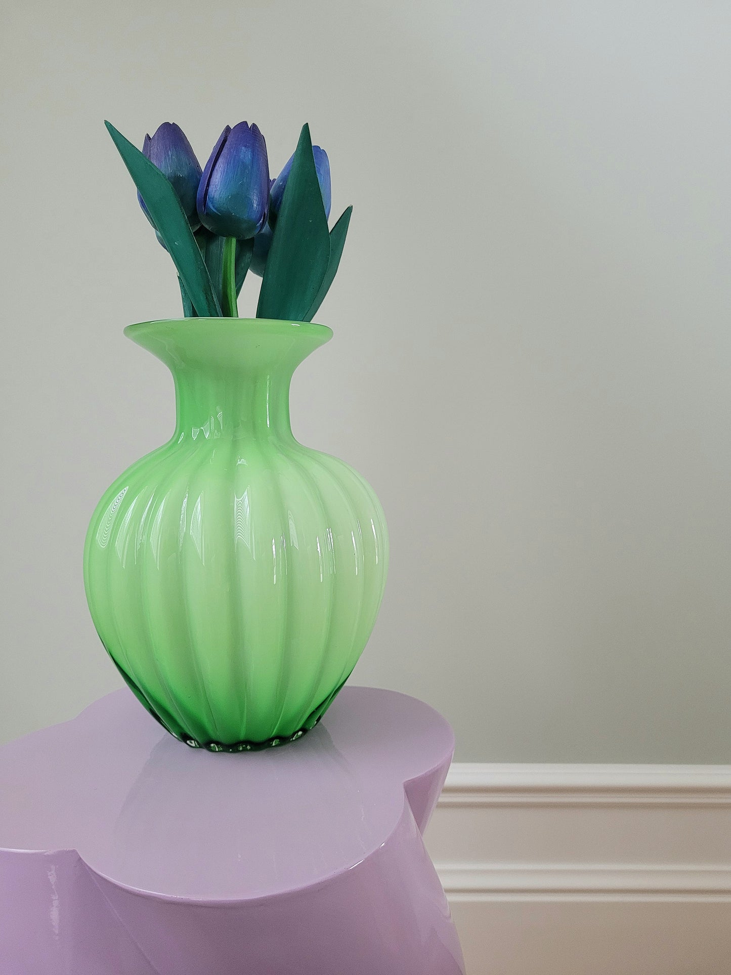 full view of a vibrant green glass vase with wooden tulips on a purple side table