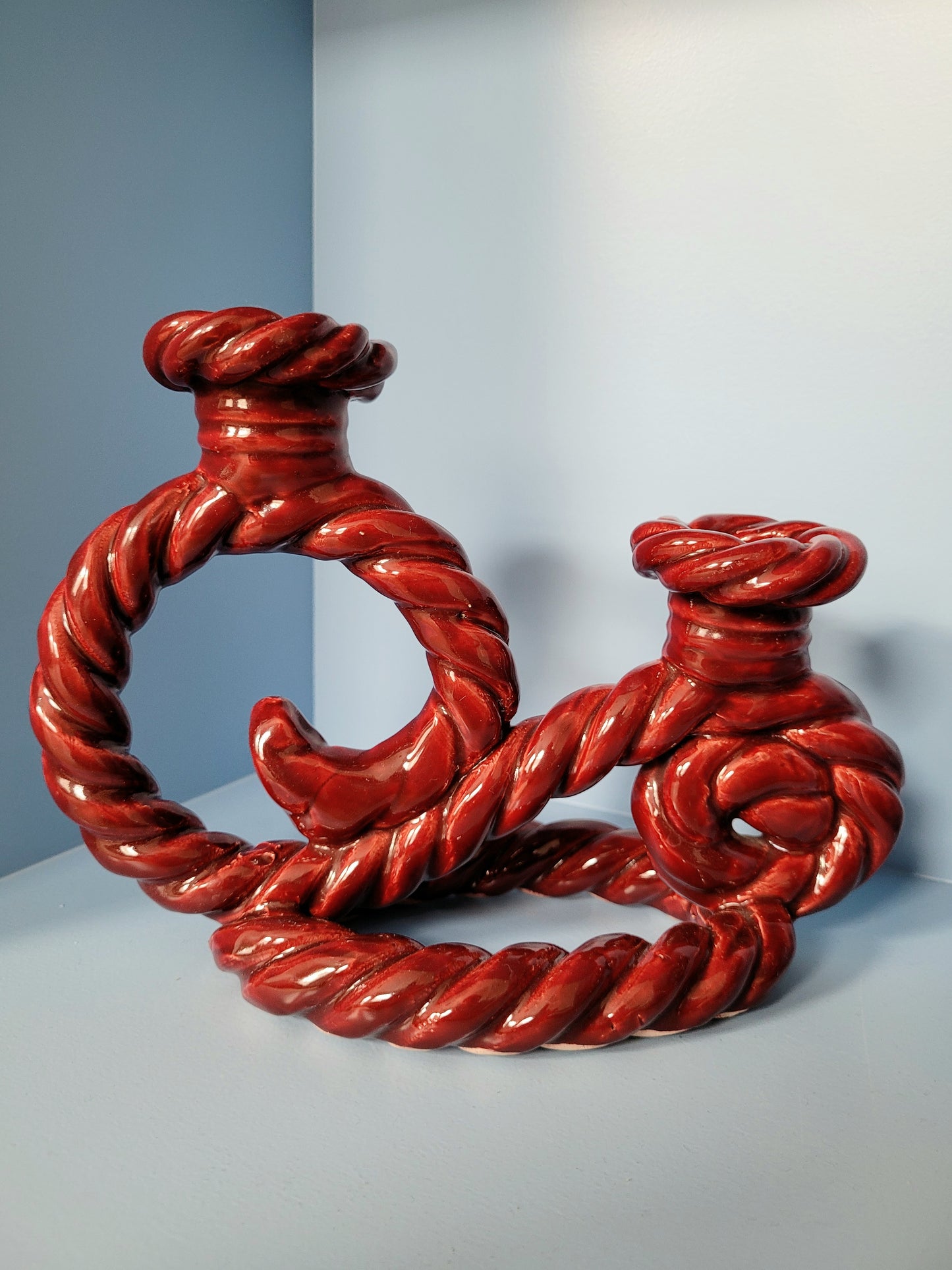 front view of a vintage red twisted ceramic candle holder in a blue cabinet