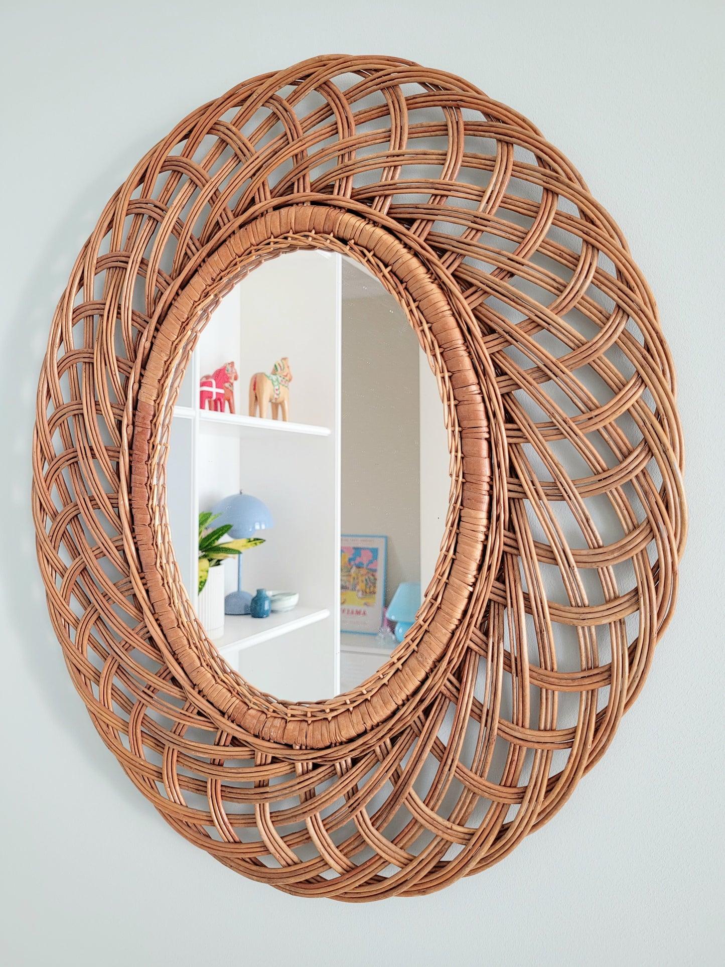 side view of a mid century large oval wall mirror next to filled colourful cabinets