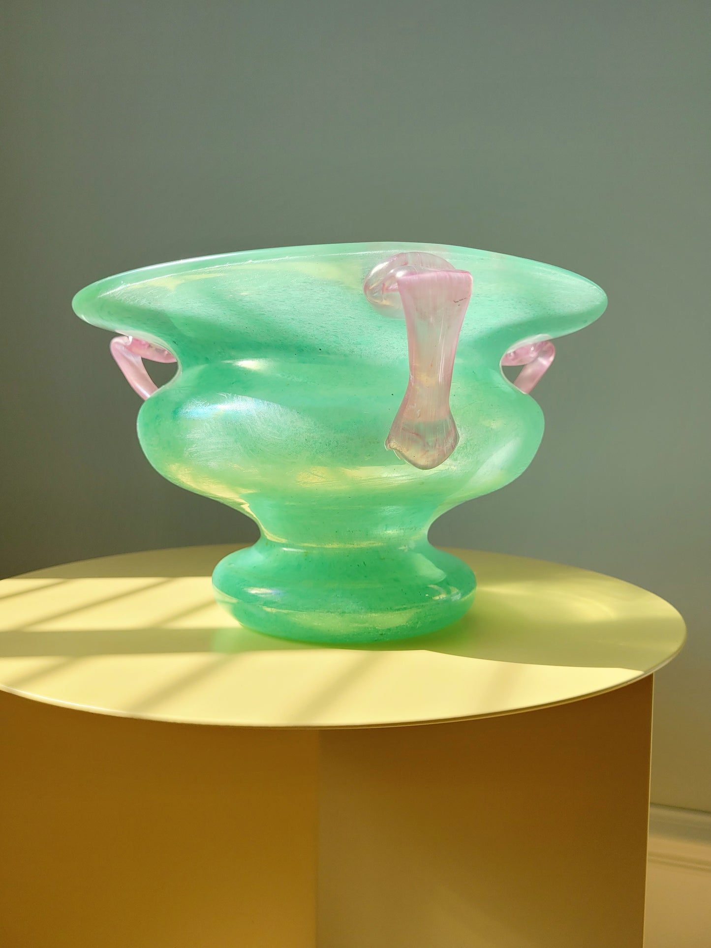 side view of a scavo Murano glass amphora vase in green and pink on a yellow side table