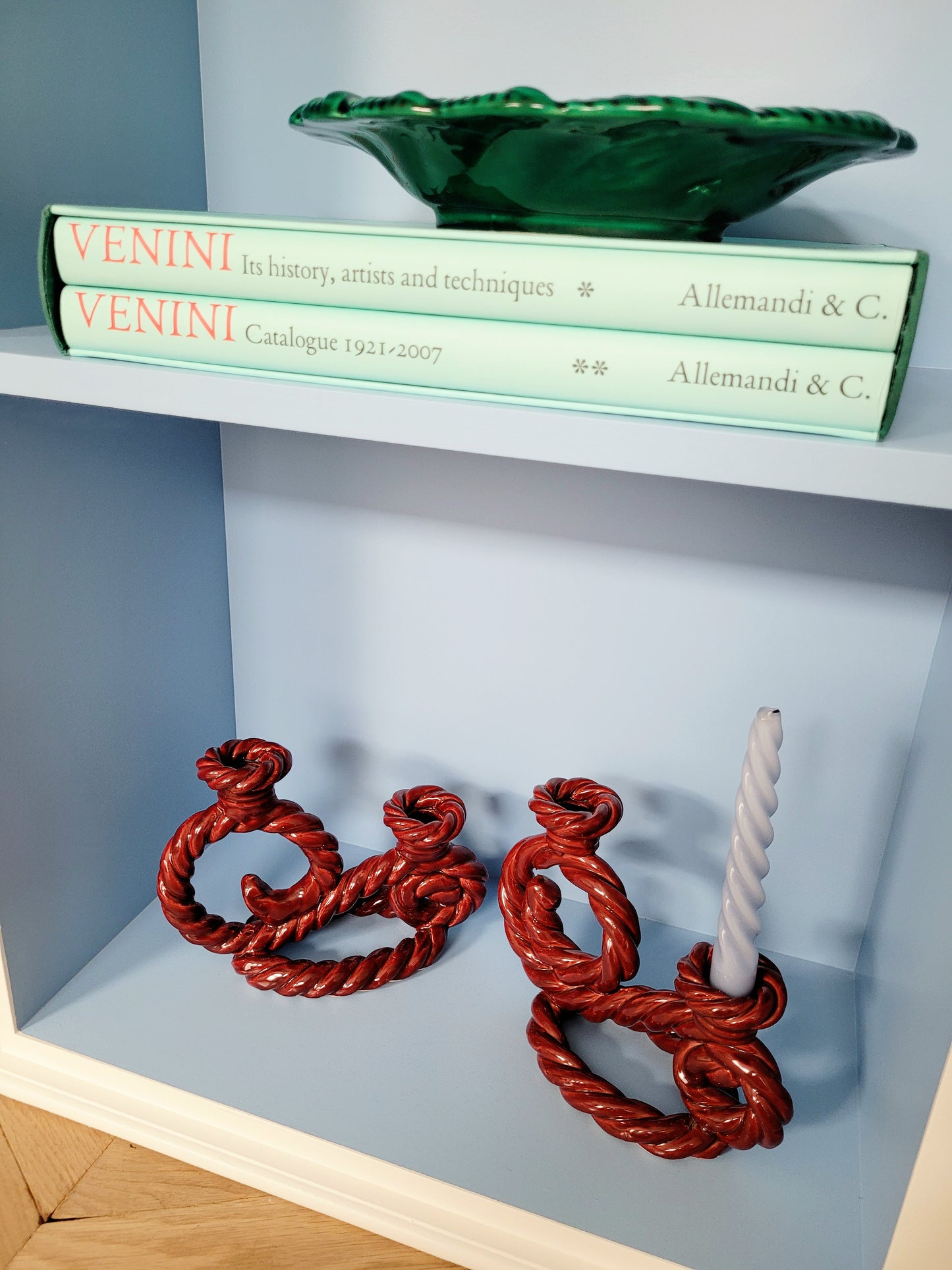 full view of two vintage red twisted ceramic candle holders in a blue cabinet