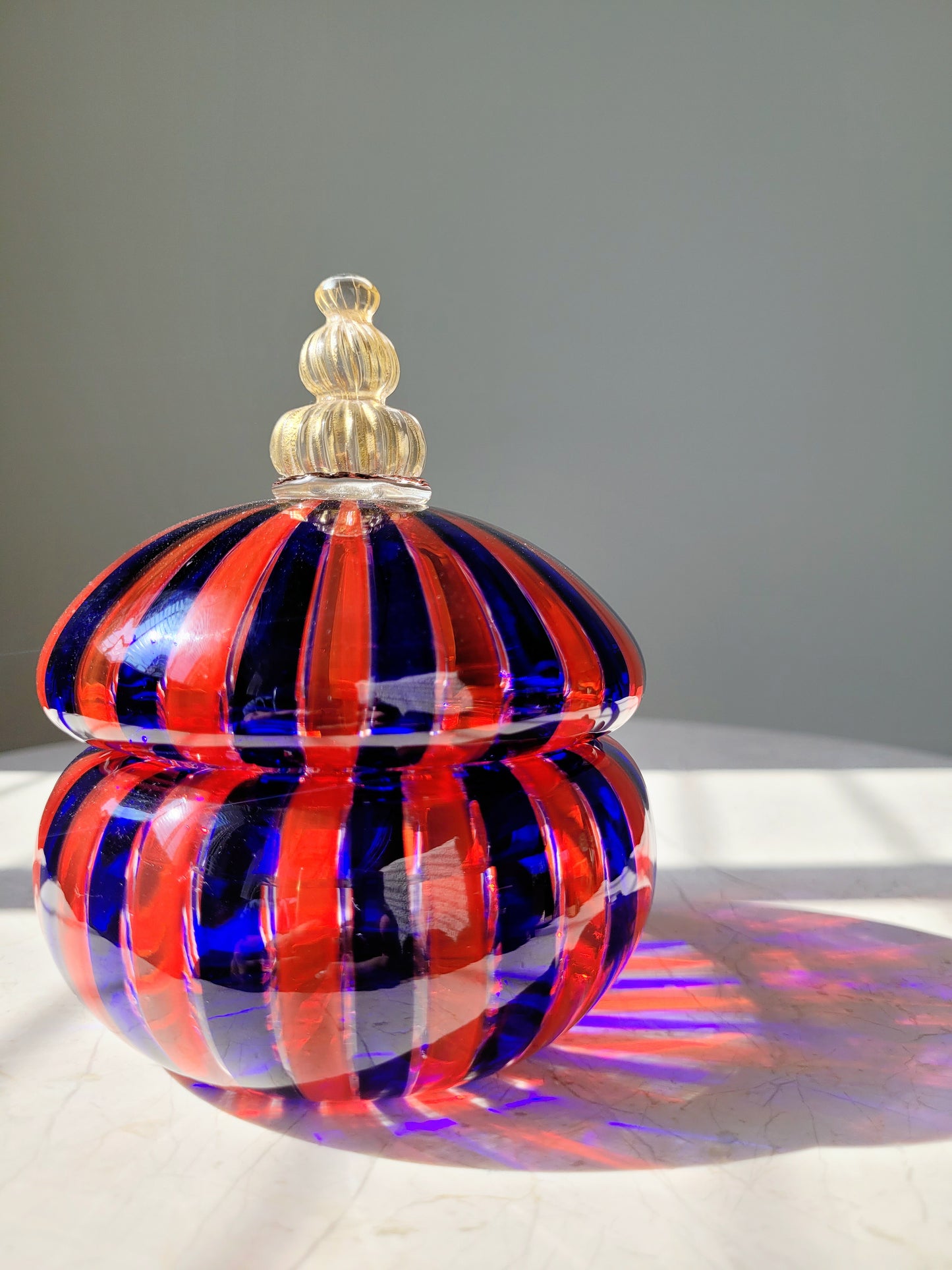 front view of a handcrafted vintage striped Murano bonbonniere in red blue and gold