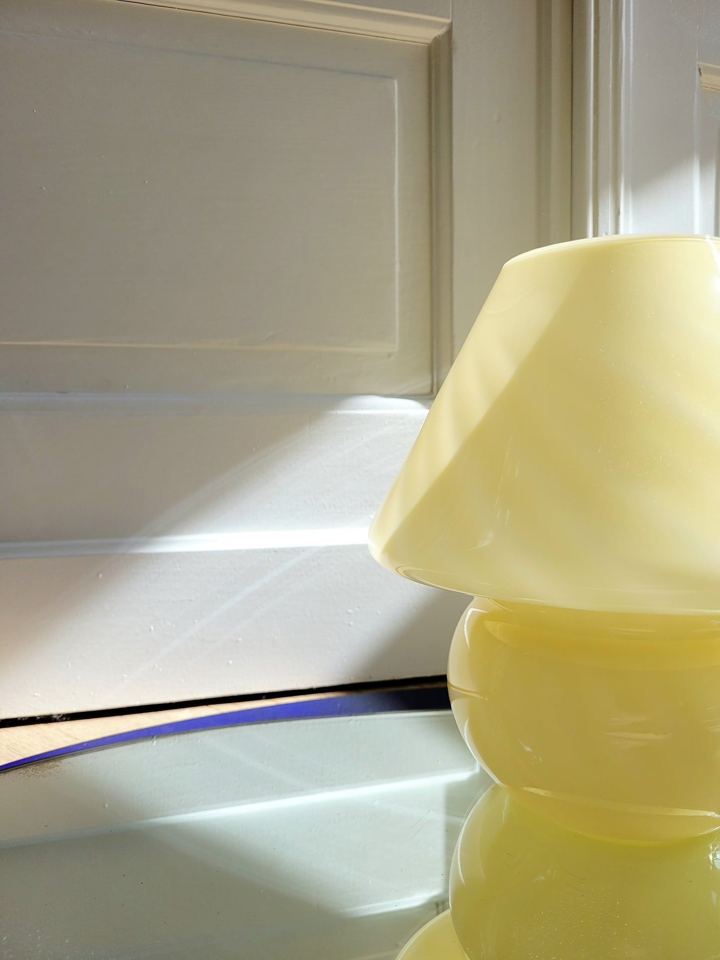 detail of an ochre yellow swirl Murano mushroom table lamp on a mirror with cobalt blue edging.