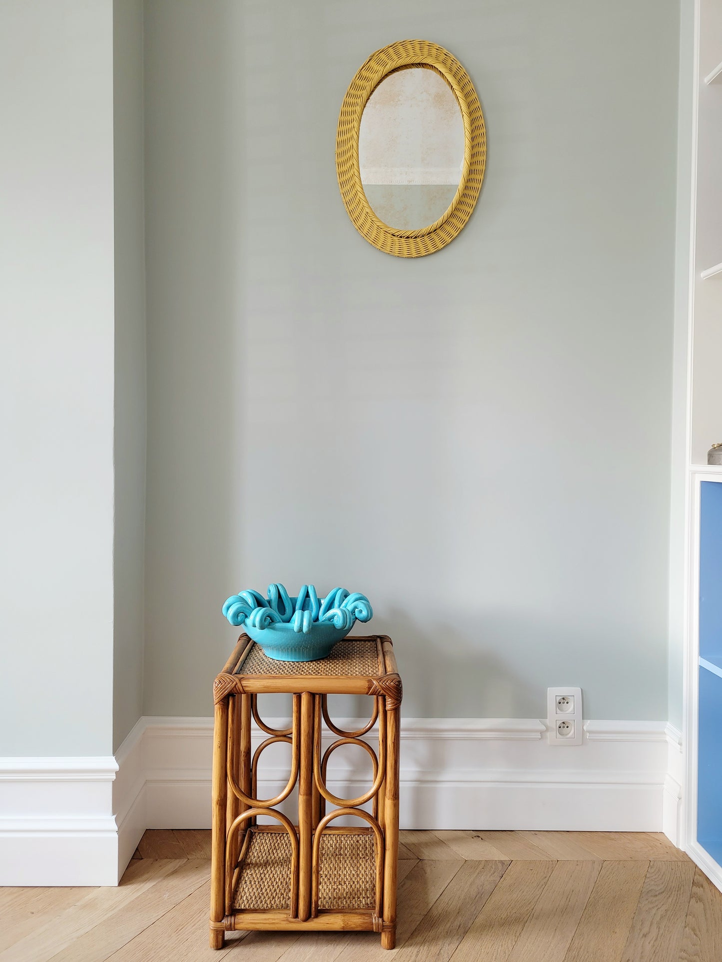 full view of a striking turquoise ceramic serving bowl on a bamboo side table and yellow mirror on wall