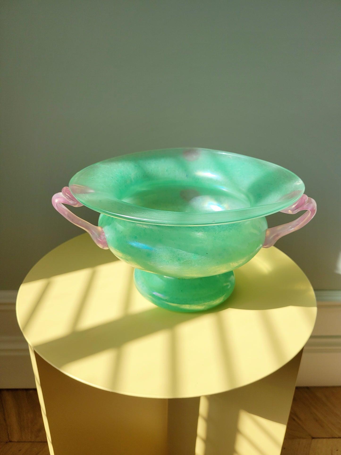 top view of a scavo Murano glass amphora vase in green and pink on a yellow side table