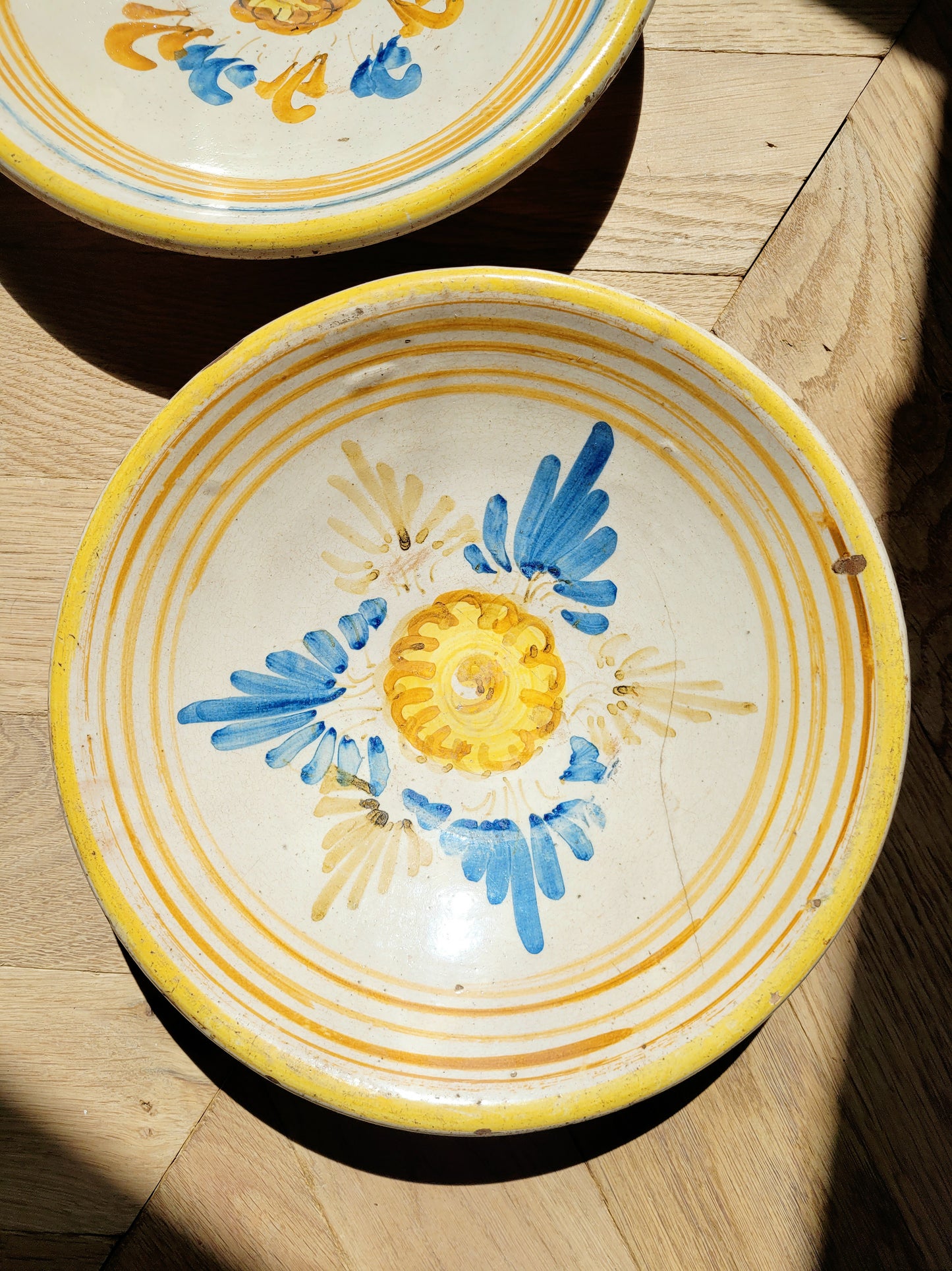 an antique ceramic (wall) plate, adorned in vibrant blue and yellow hues with a stunning flower pattern on a parquet floor