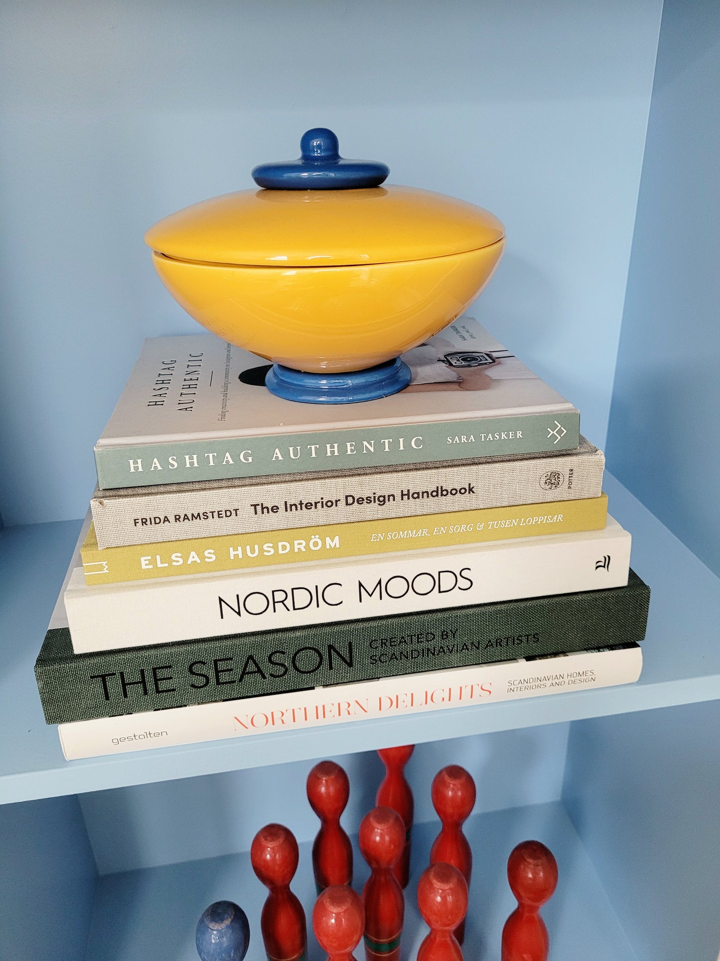 front view of a ceramic jar in blue and yellow on a stack of interior books