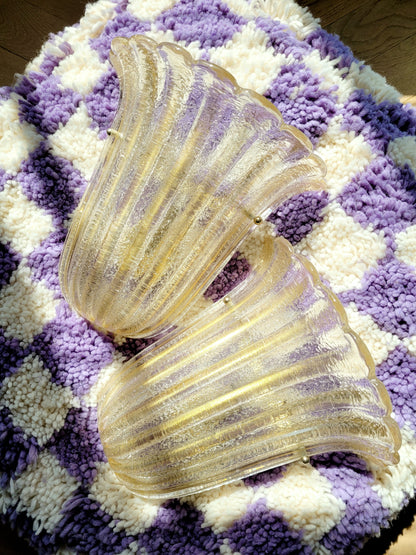 top view of a pair of Barovier & Toso Murano glass wall lamps with a leaf design. The lamps are placed on a pouf with a purple and white checkerboard pattern.