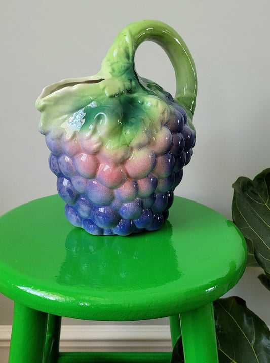 front view of a barbotine ceramic wine pitcher with grapes on a green side table