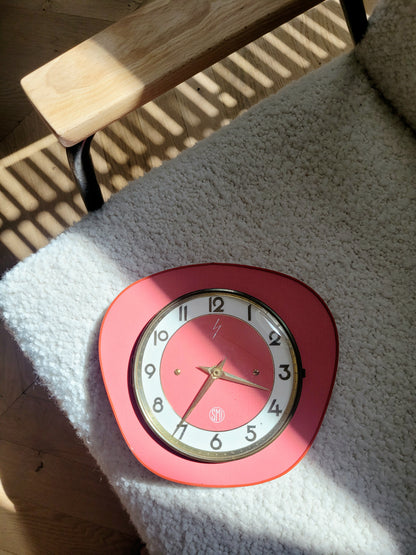 full view of a red wall clock of the French brand SMI in formica with a brass ring and curved glass on top of a chair