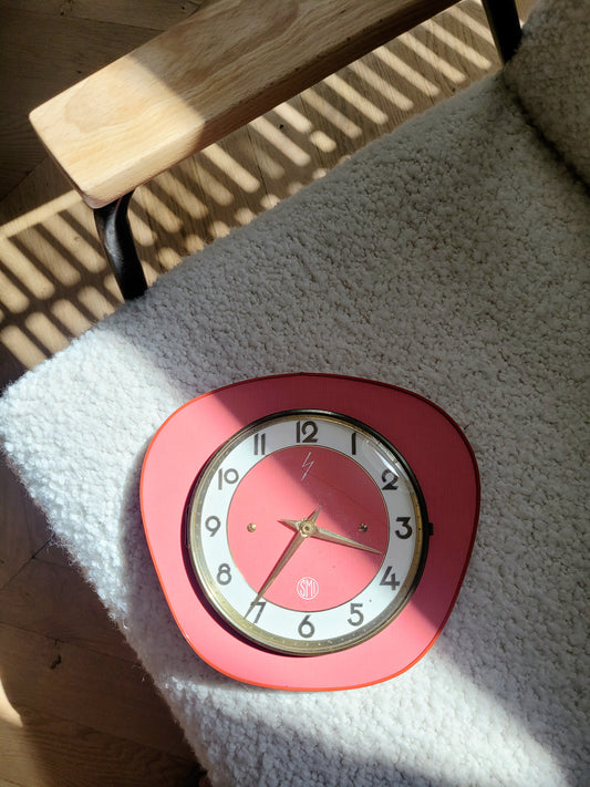 full view of a red wall clock of the French brand SMI in formica with a brass ring and curved glass on top of a chair