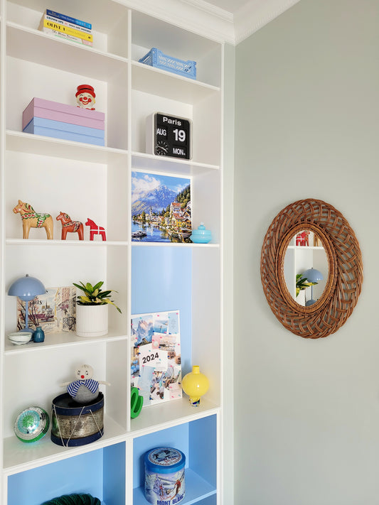 side view of a mid century large oval wall mirror next to filled colourful cabinets