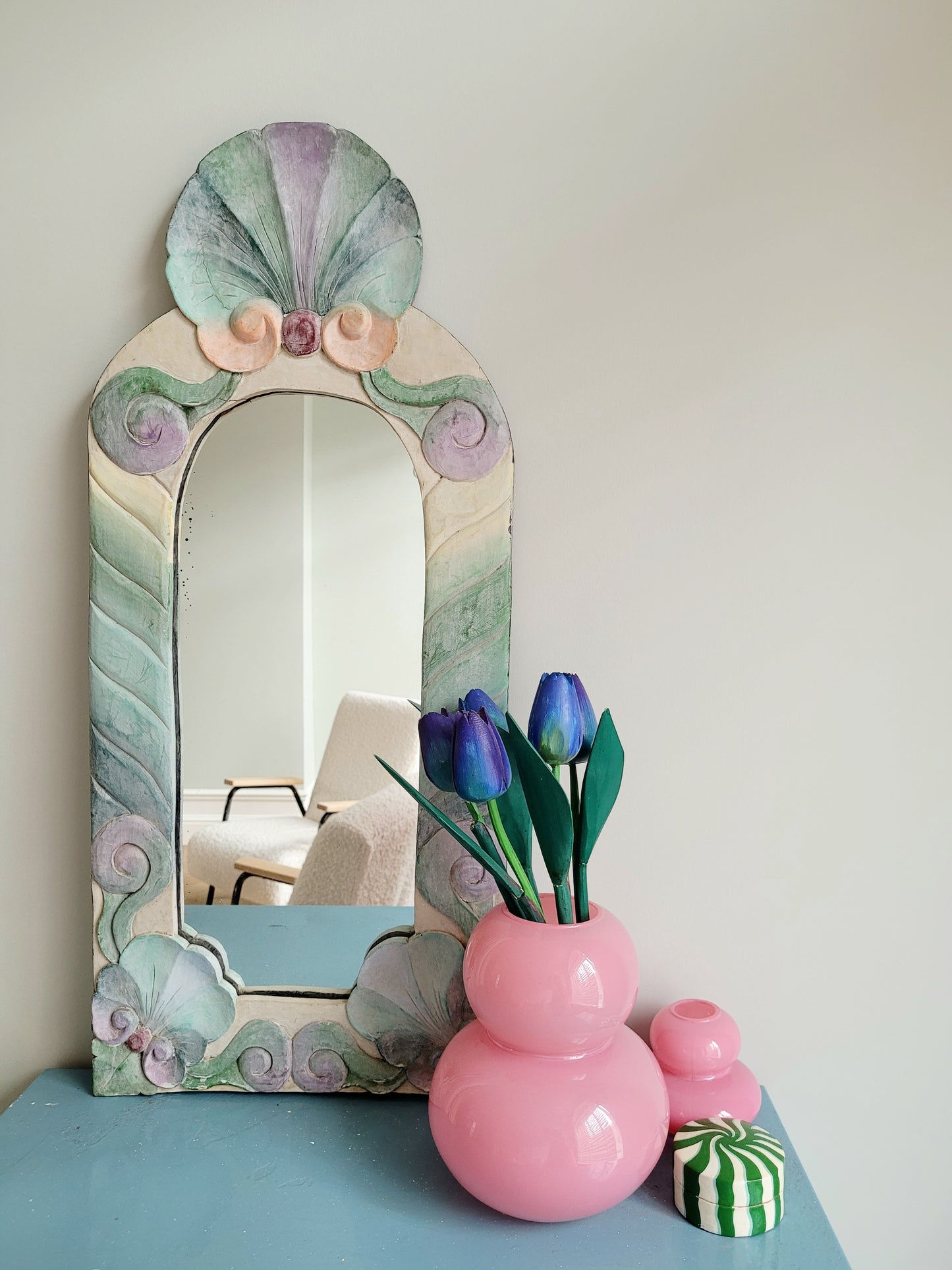 front view of a pastel coloured wooden wall mirror with flower design next to a pink vase with wooden tulips
