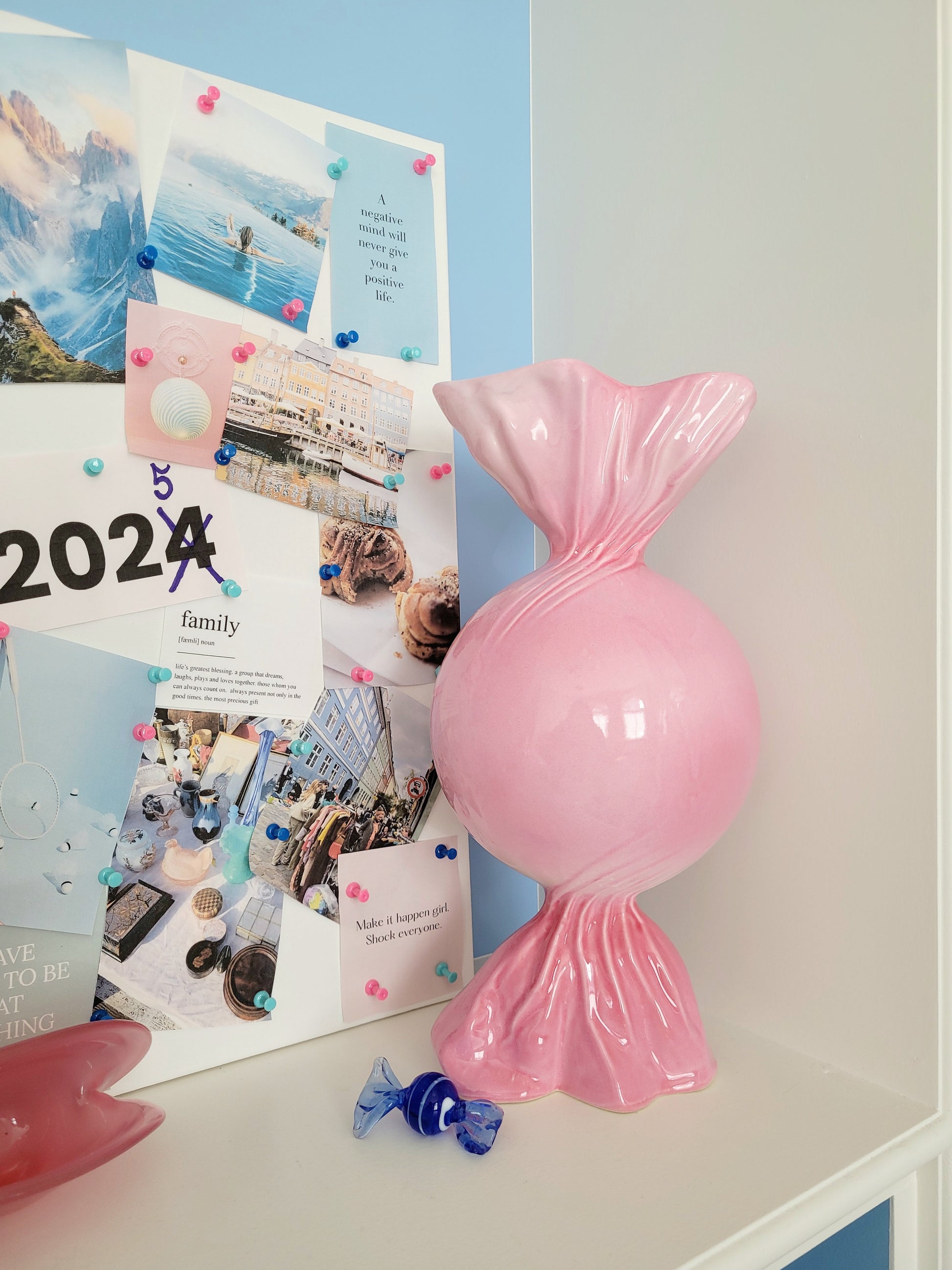 front view of a pink ceramic candy bonbon vase with a vision board next to it and a small Murano candy in the front