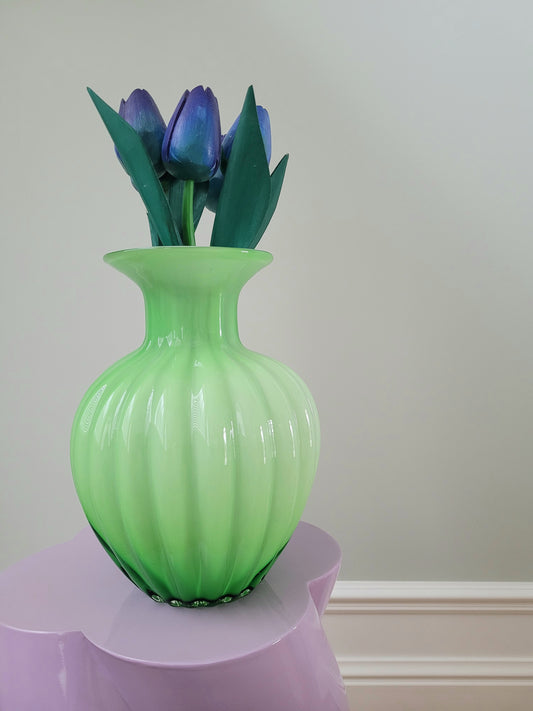 full view of a vibrant green glass vase with wooden tulips on a purple side table