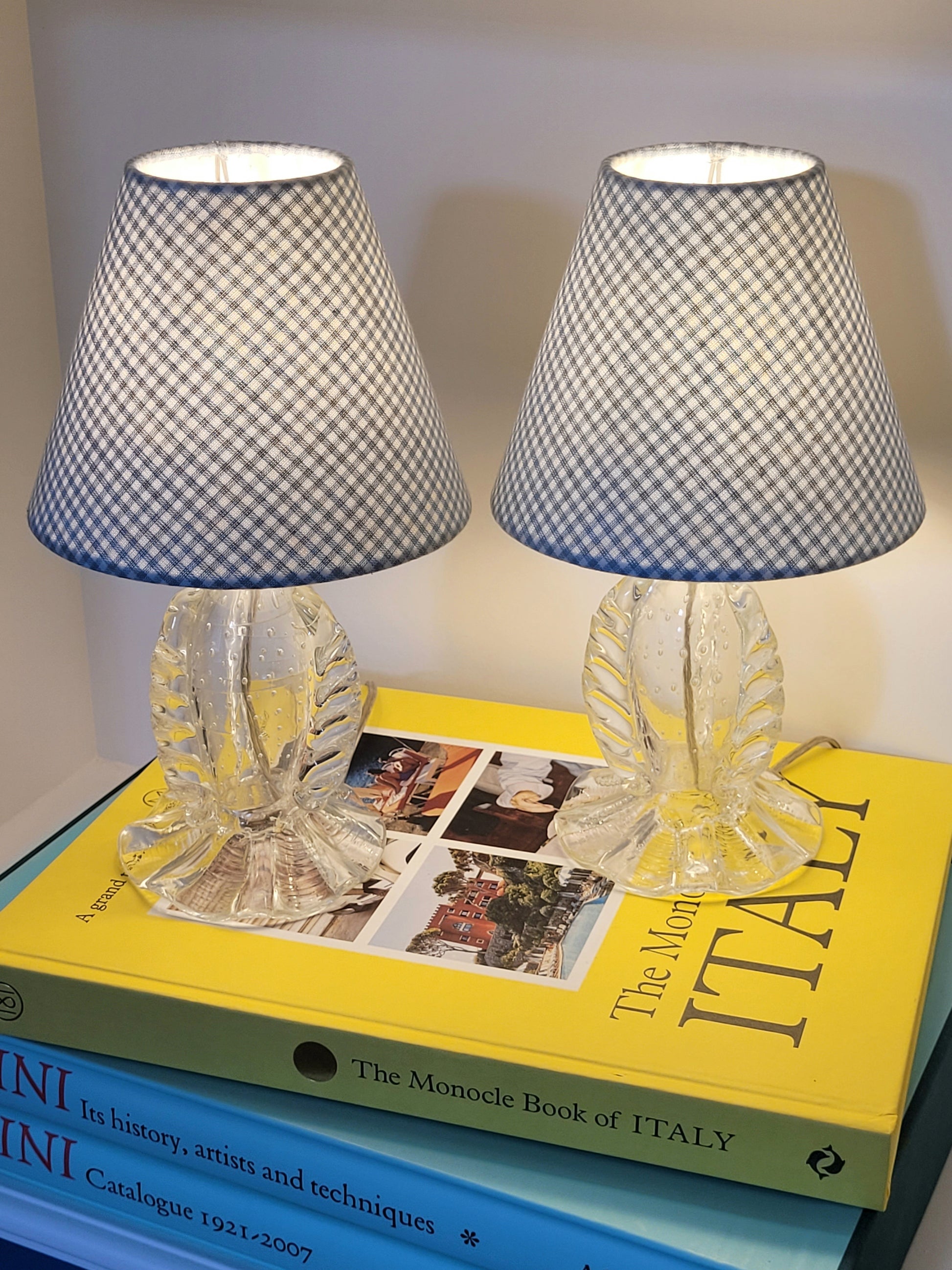 front view of a rare pair of vintage clear Murano table lamps with shades stacked on books illuminated