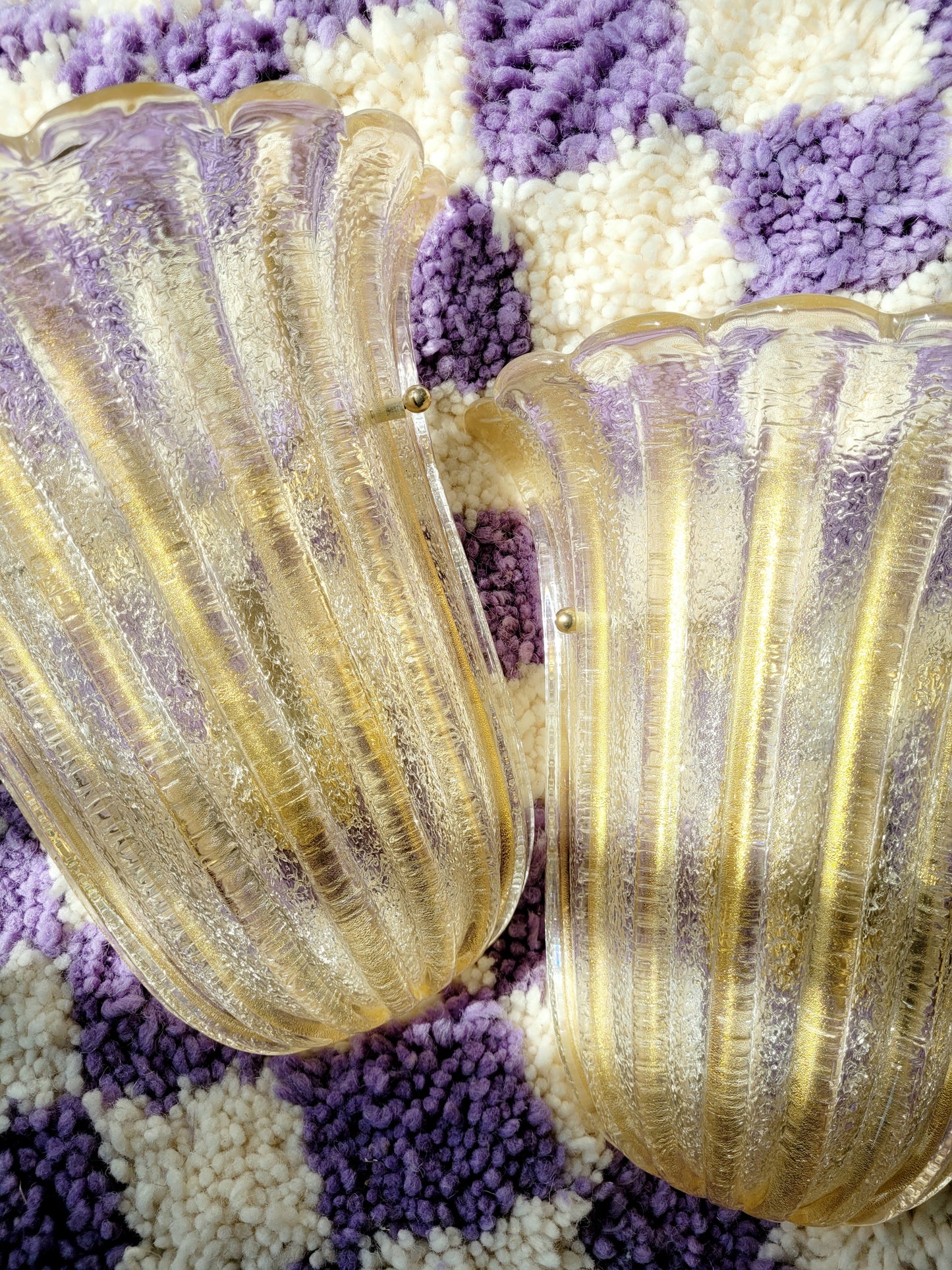 detail of a pair of Barovier & Toso Murano glass wall lamps with a leaf design. The lamps are placed on a pouf with a purple and white checkerboard pattern.