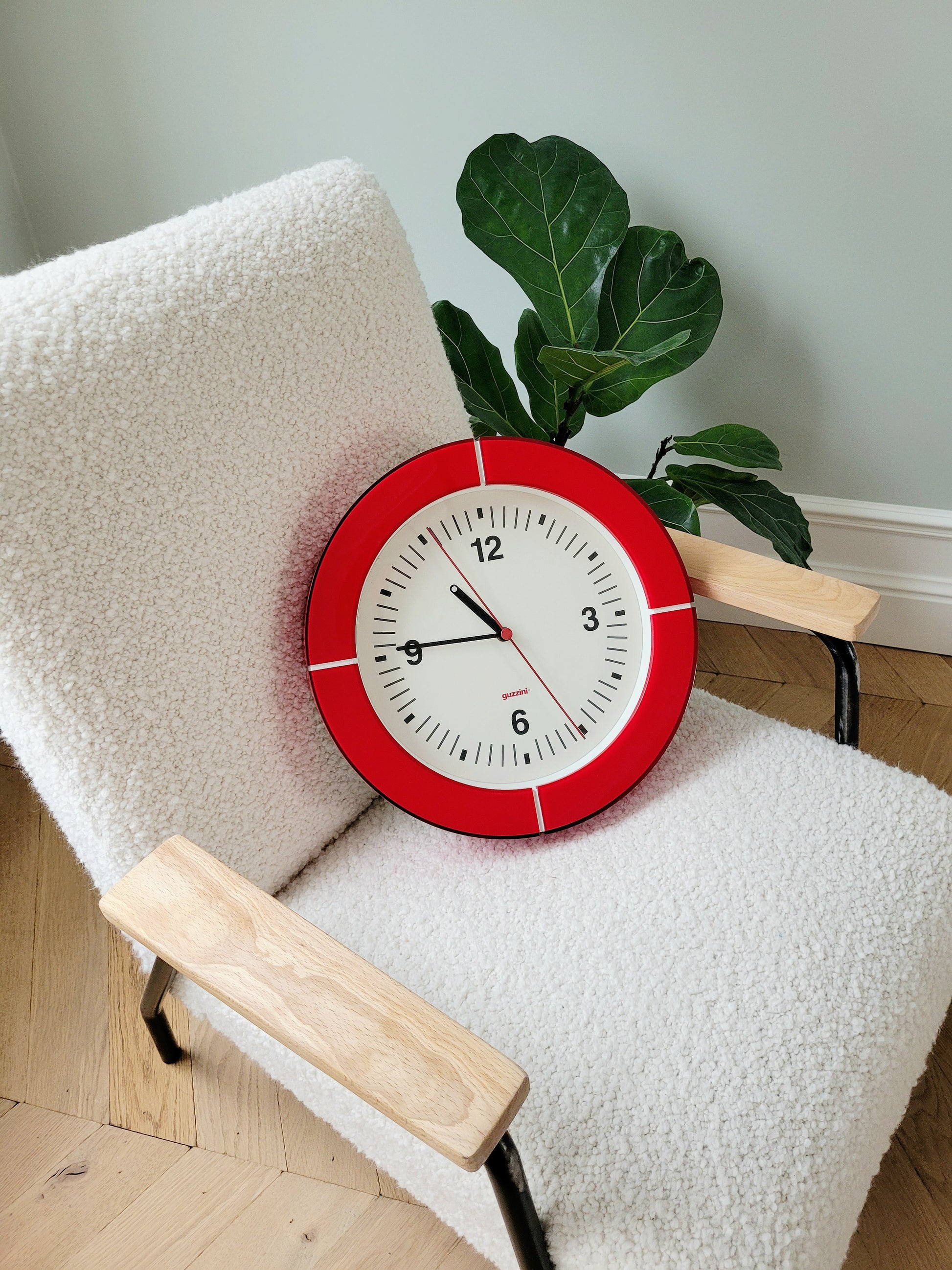 full view of a Guzzini acrylic red wall clock on an armchair