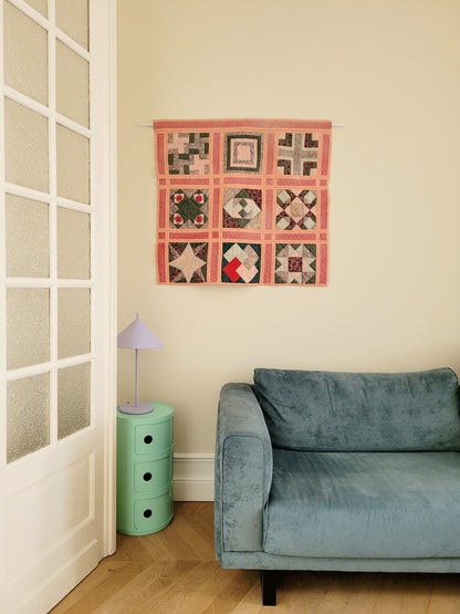 full view of a pink and green vintage handmade patchwork quilt with unique geometric pattern against a yellow wall and above a green side table with purple table lamp and teal sofa