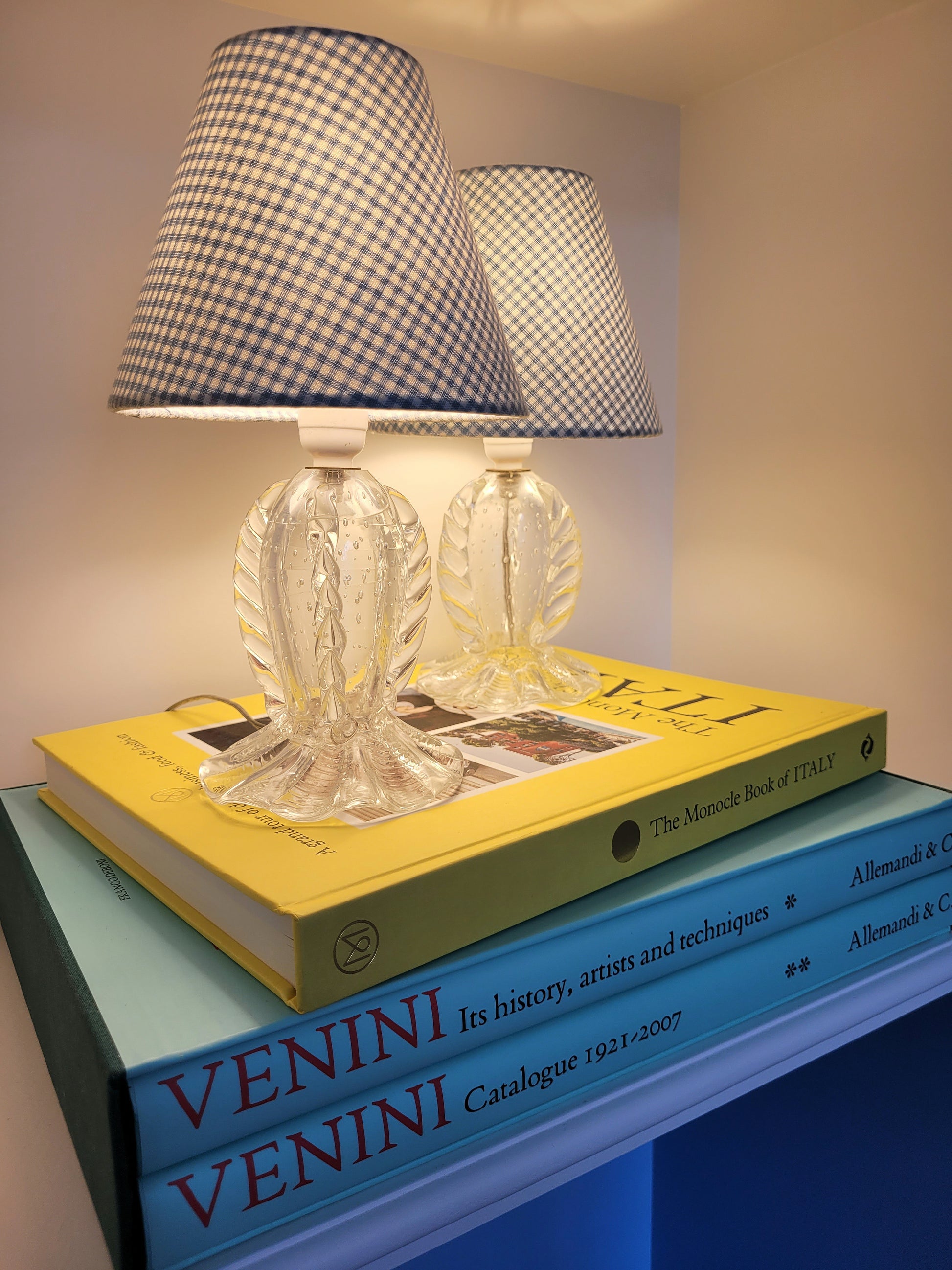 side view of a rare pair of vintage clear Murano table lamps with shades stacked on books illuminated