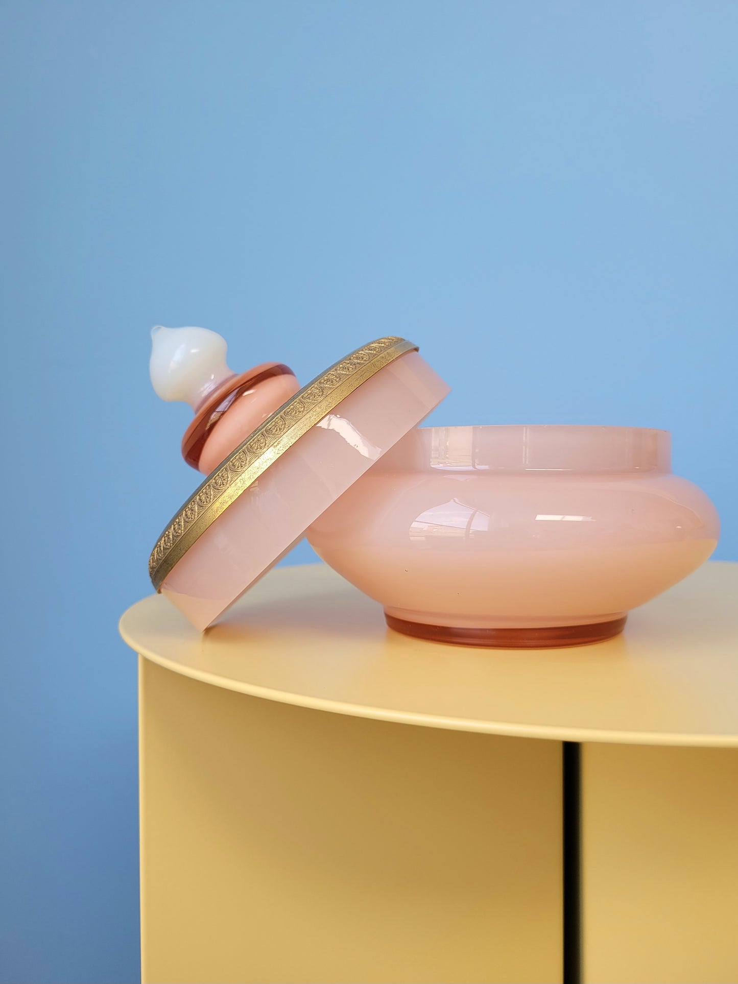 front view of a vintage opal pink glass bonbonniere with lid on a yellow side table
