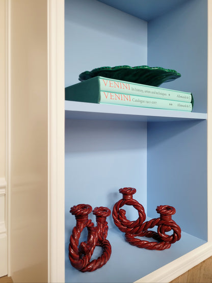 side view of two vintage red twisted ceramic candle holders in a blue cabinet