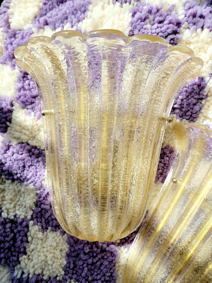 top view of a pair of Barovier & Toso Murano glass wall lamps with a leaf design. The lamps are placed on a pouf with a purple and white checkerboard pattern.