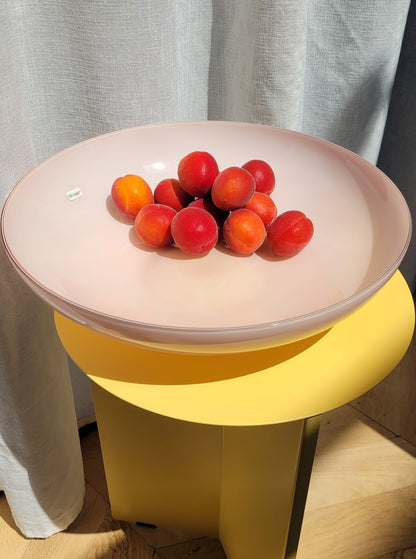 top view of a large vintage opal pink Murano bowl filled with fruit on a yellow side table