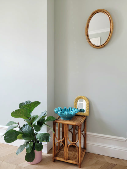 full view of an oval wall mirror in natural bamboo with a side table