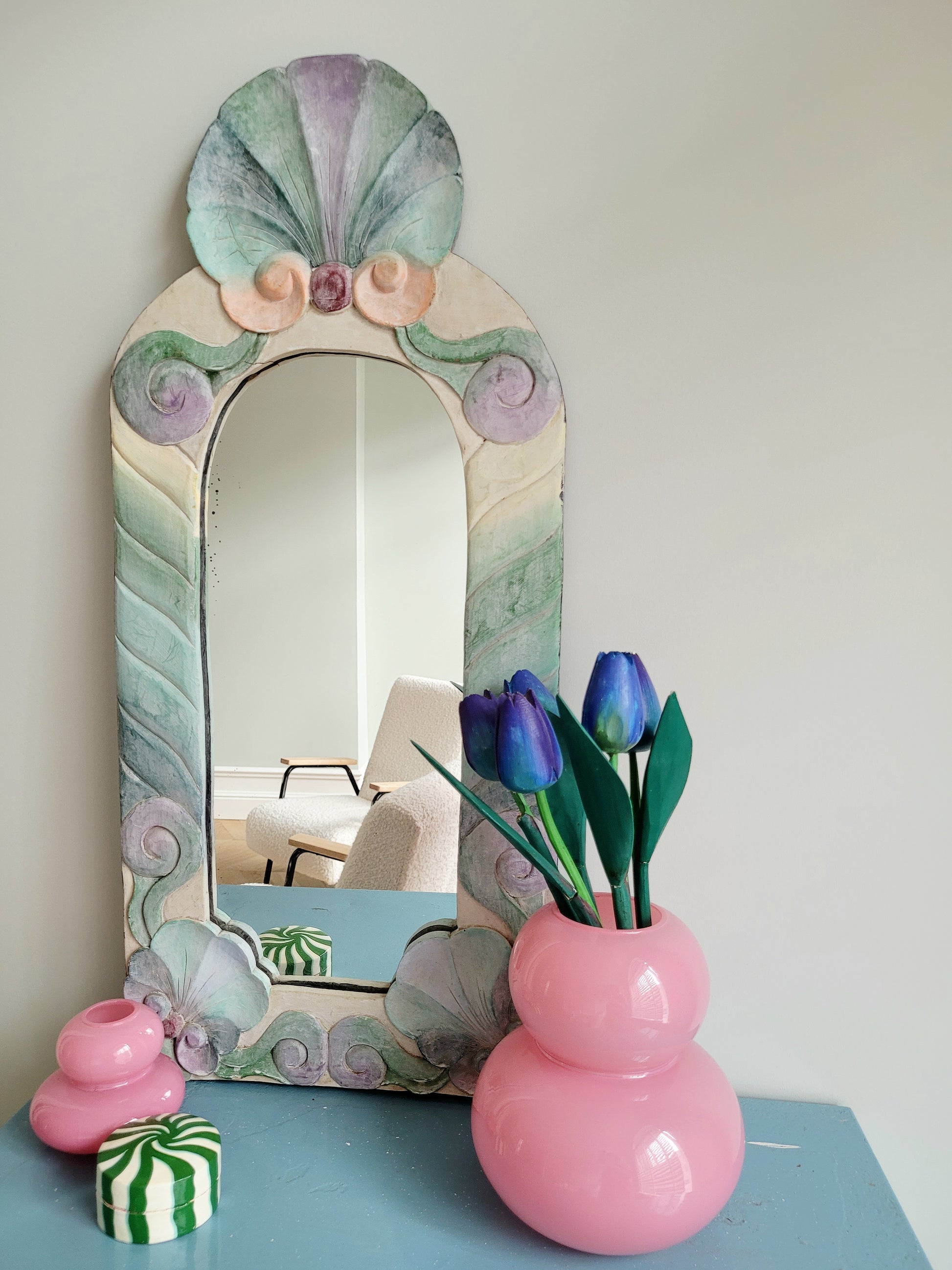 front view of a pastel coloured wooden wall mirror with flower design next to a pink vase with wooden tulips