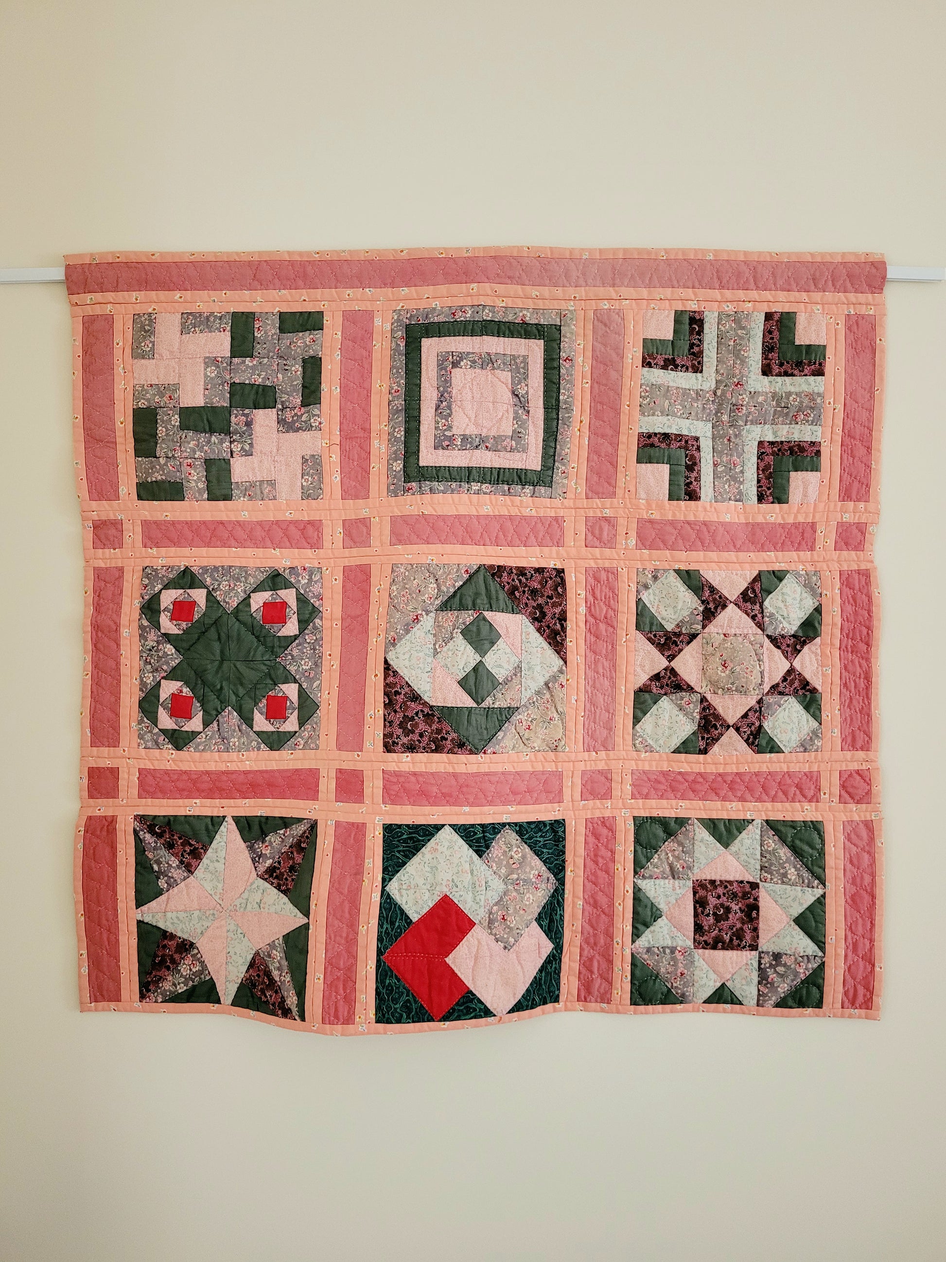 detail of a pink and green vintage handmade patchwork quilt with unique geometric pattern against a yellow wall 