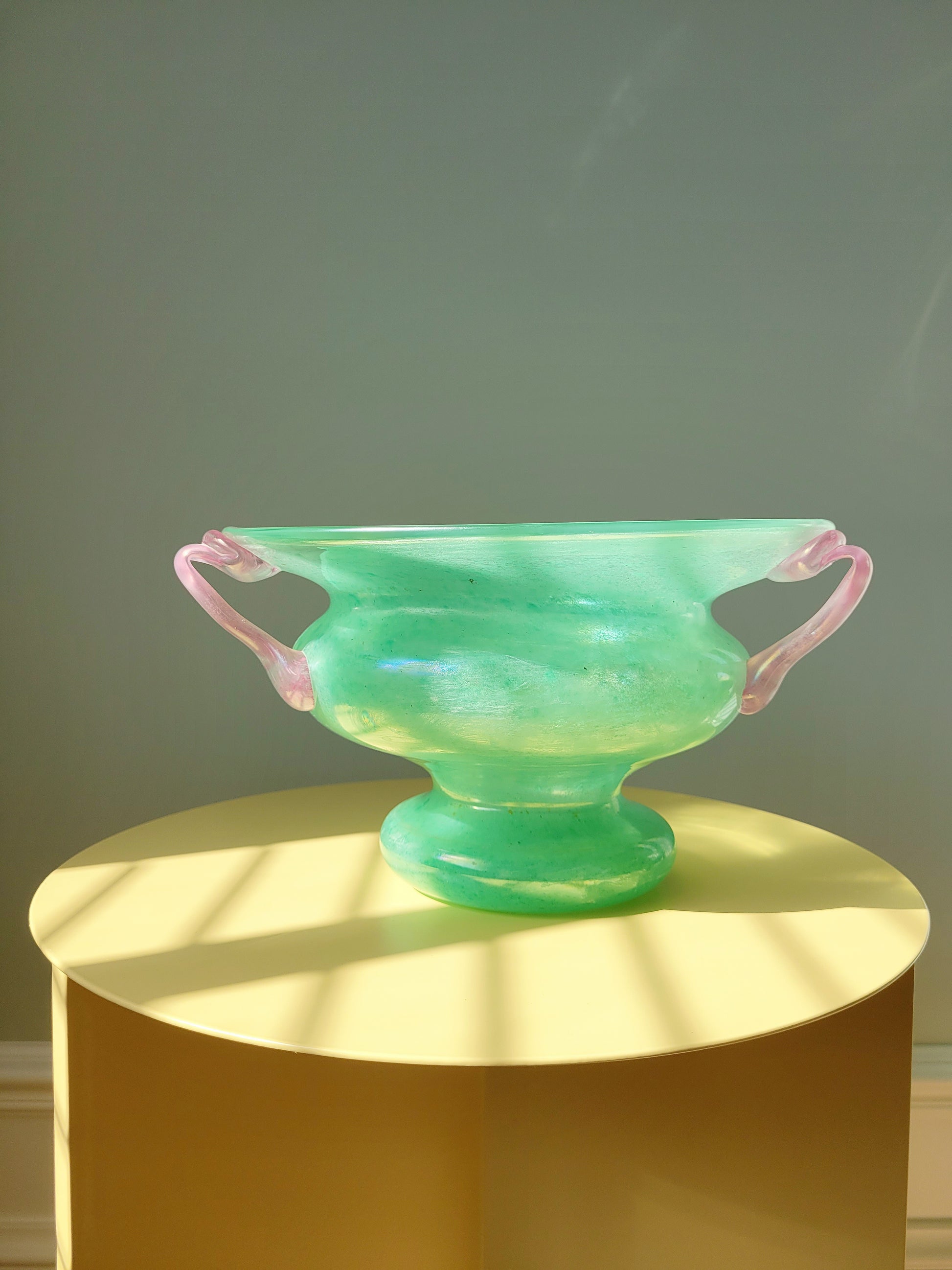 full view of a scavo Murano glass amphora vase in green and pink on a yellow side table