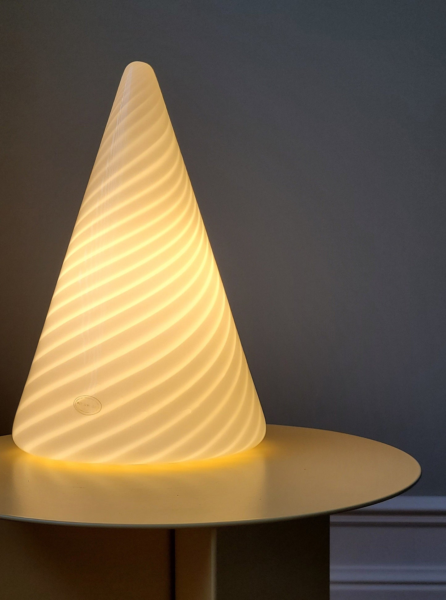 front view of an illuminated vintage Murano cone lamp with white and translucent swirl on a yellow side table
