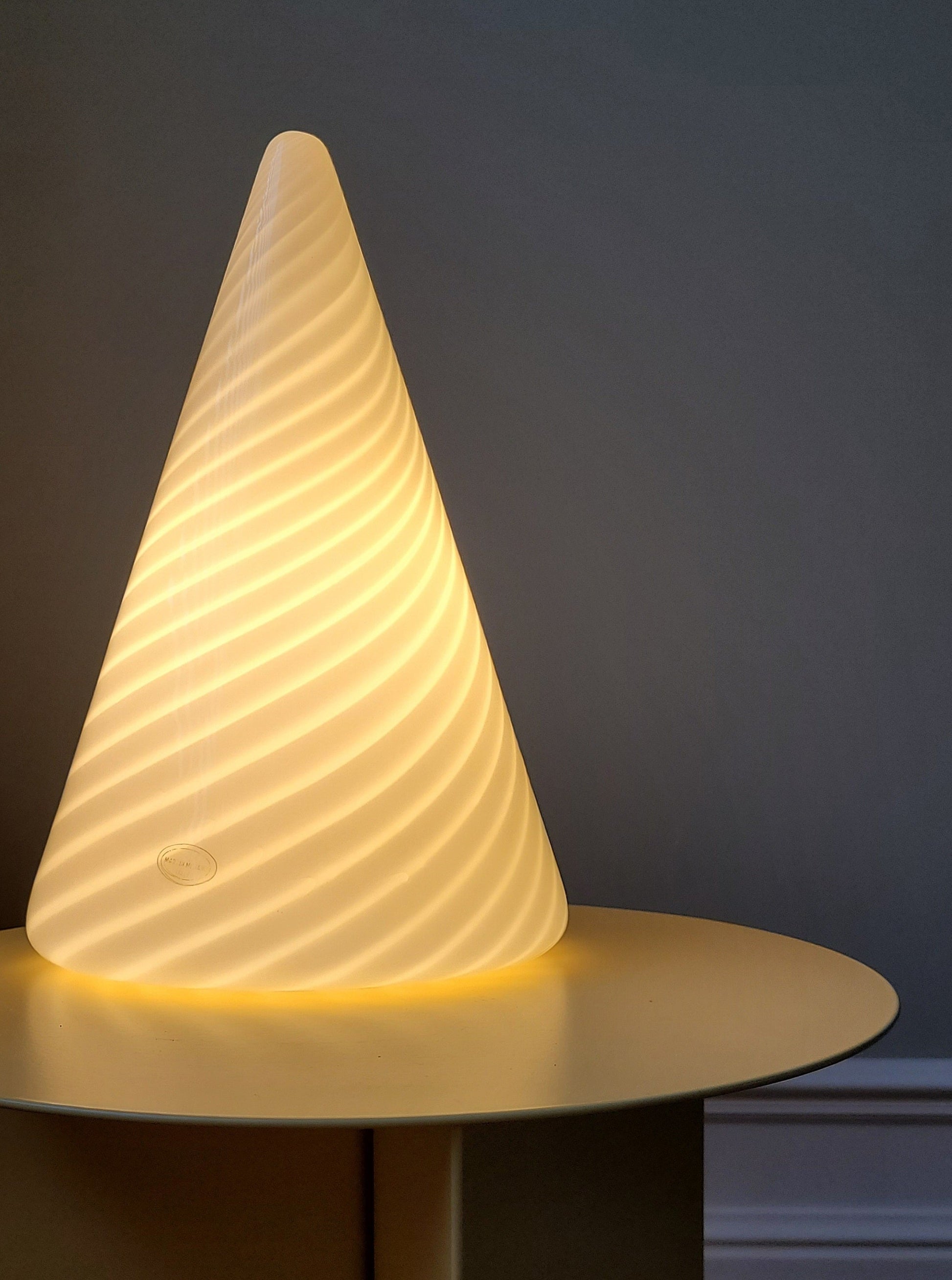 front view of an illuminated vintage Murano cone lamp with white and translucent swirl on a yellow side table