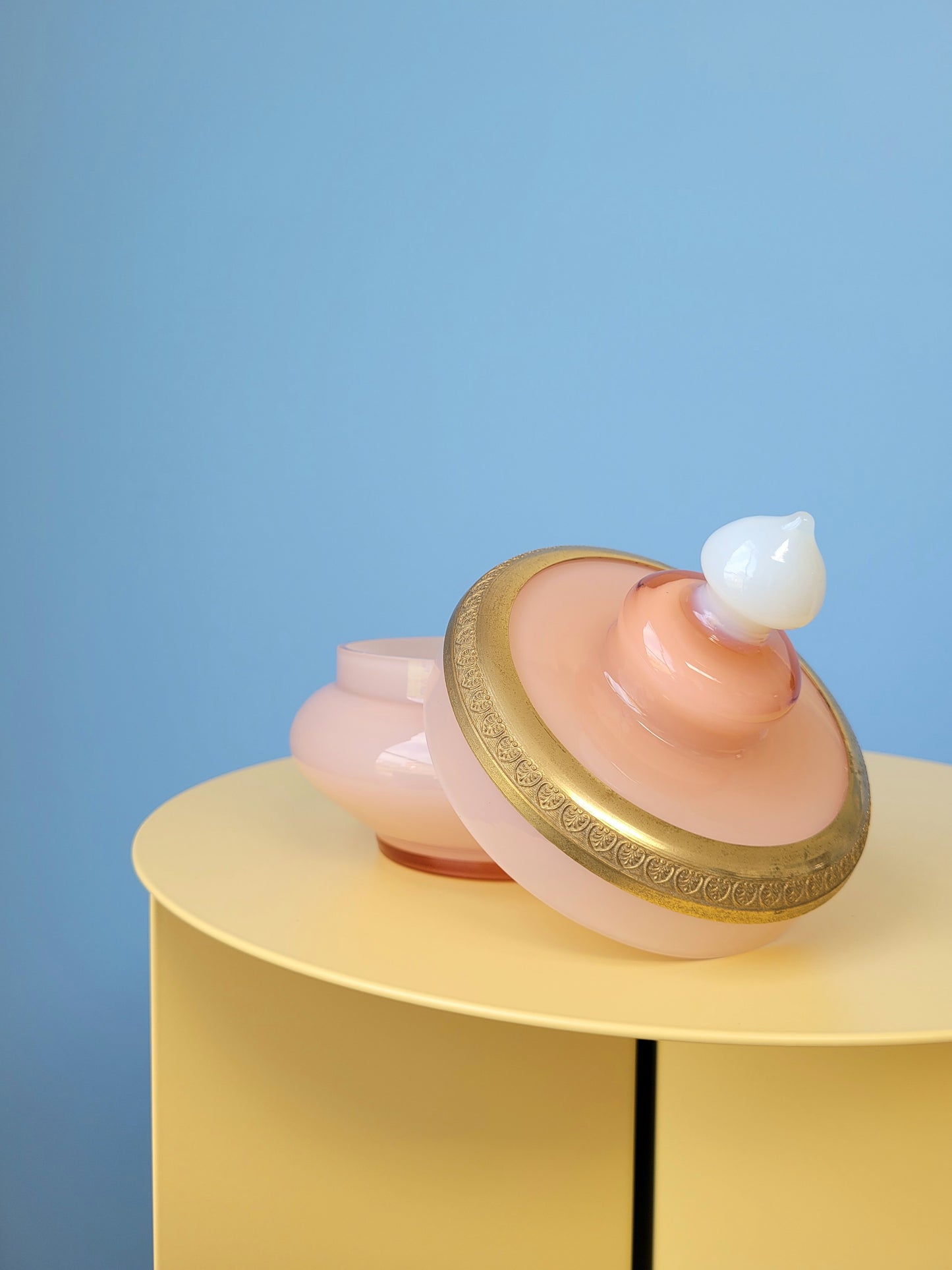side view of a vintage opal pink glass bonbonniere with lid on a yellow side table