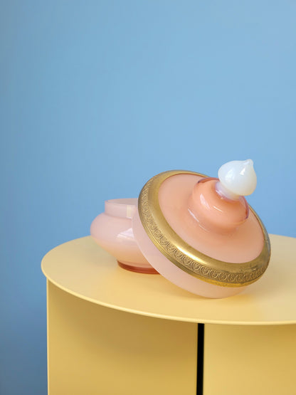 side view of a vintage opal pink glass bonbonniere with lid on a yellow side table
