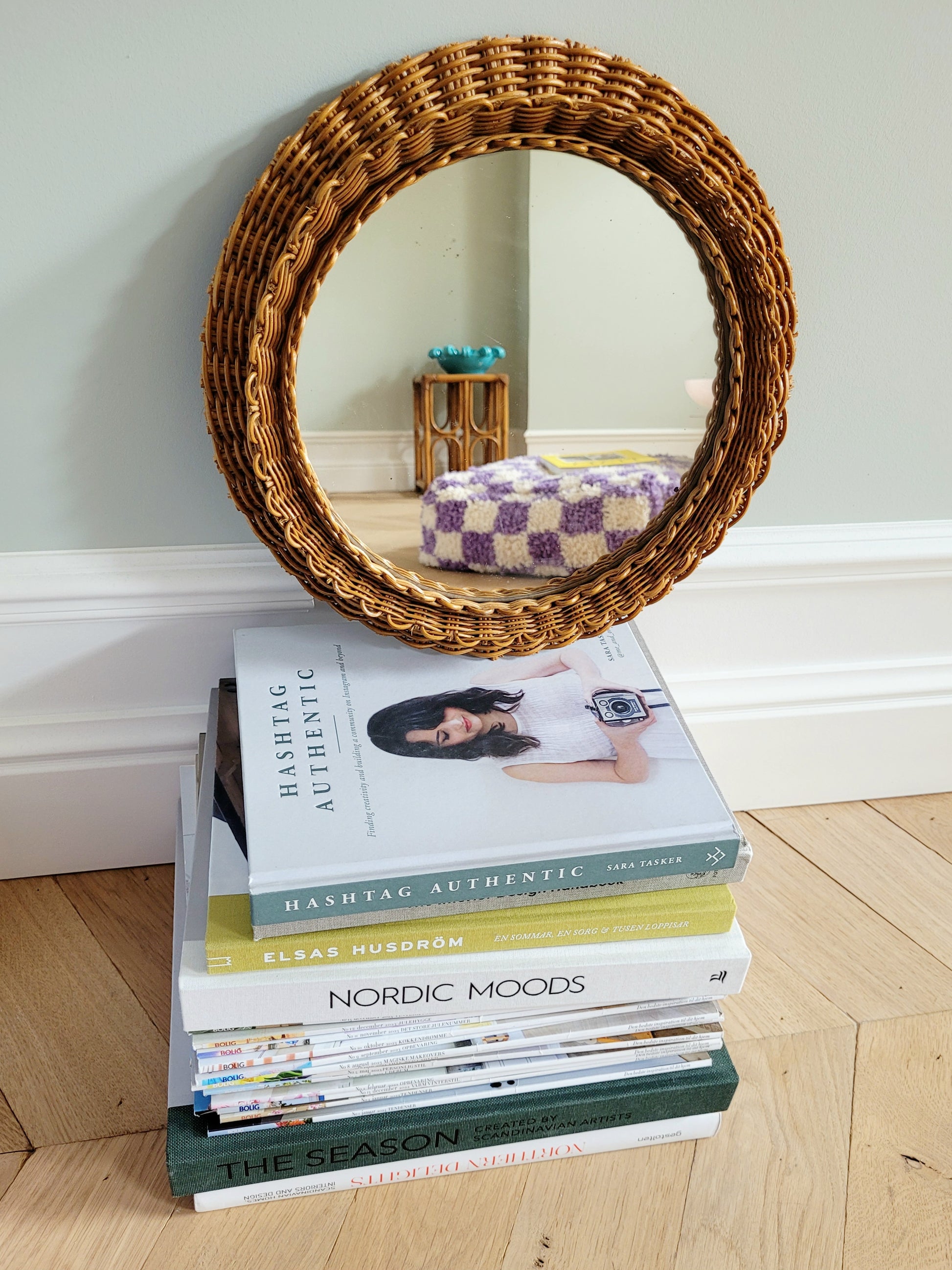 front view of a vintage woven round wall mirror stacked on top of a pile of books