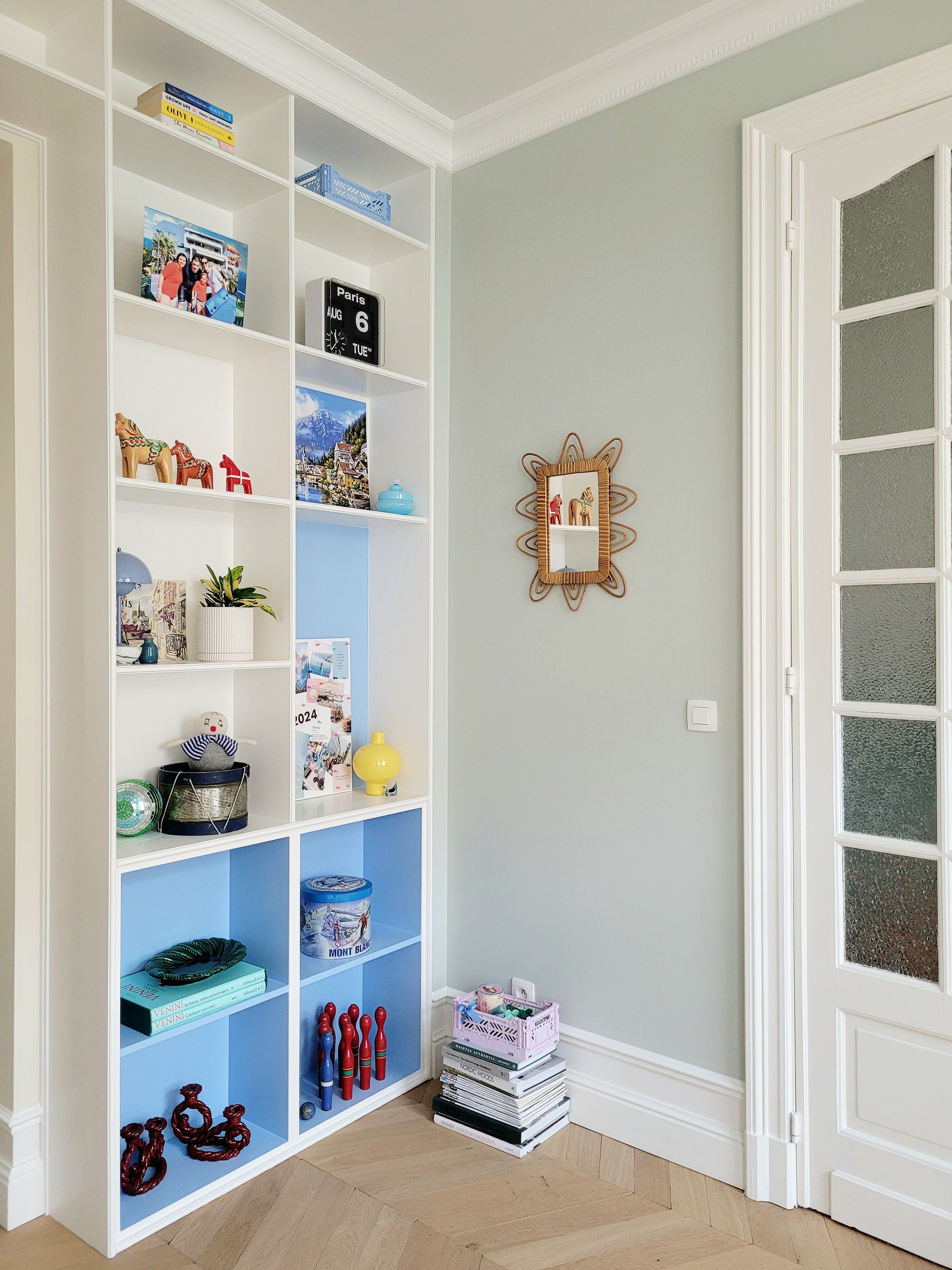full view of a playful vintage wall mirror with rattan frame next to colourful filled cabinets