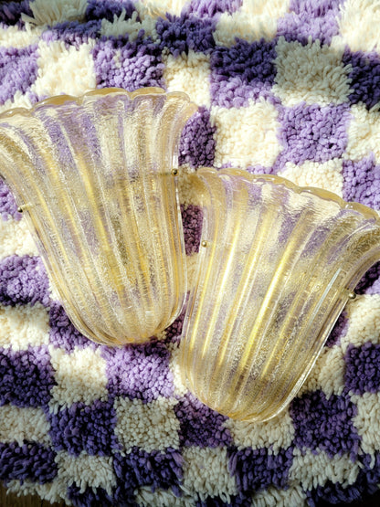 top view of a pair of Barovier & Toso Murano glass wall lamps with a leaf design. The lamps are placed on a pouf with a purple and white checkerboard pattern.