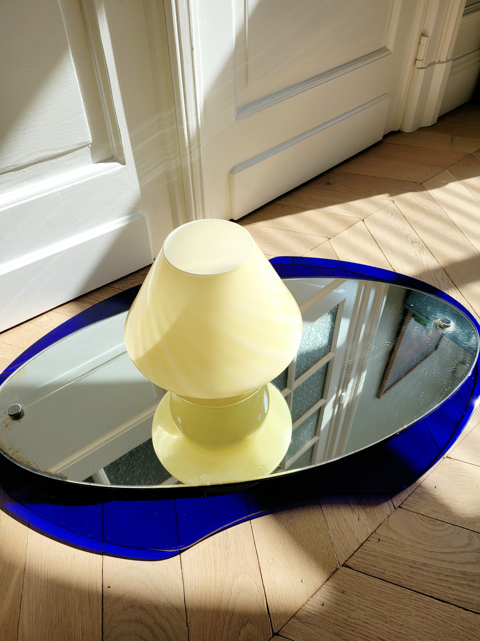 top view of an ochre yellow swirl Murano mushroom table lamp on a mirror with cobalt blue edging. 